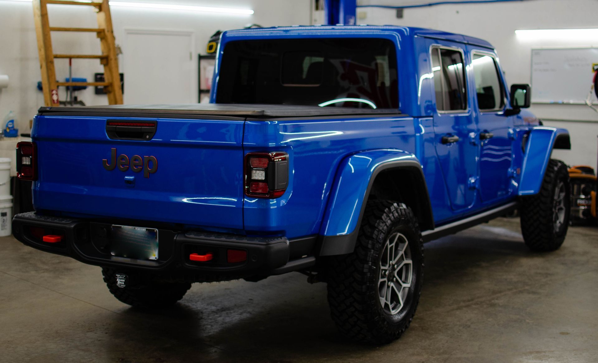 Blue Jeep Gladiator pickup truck parked indoors in a garage, rear three-quarter view