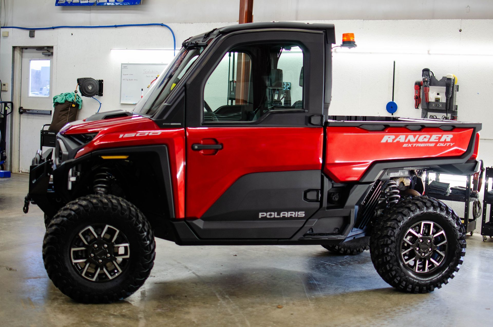 Red Polaris Ranger side-by-side utility vehicle with oversized tires in a garage.