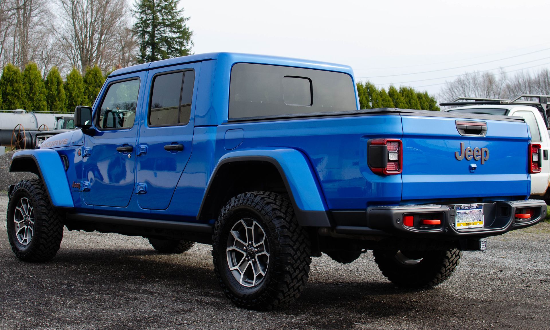 Blue Jeep Gladiator pickup truck parked outdoors on a wet lot, rear three-quarter view