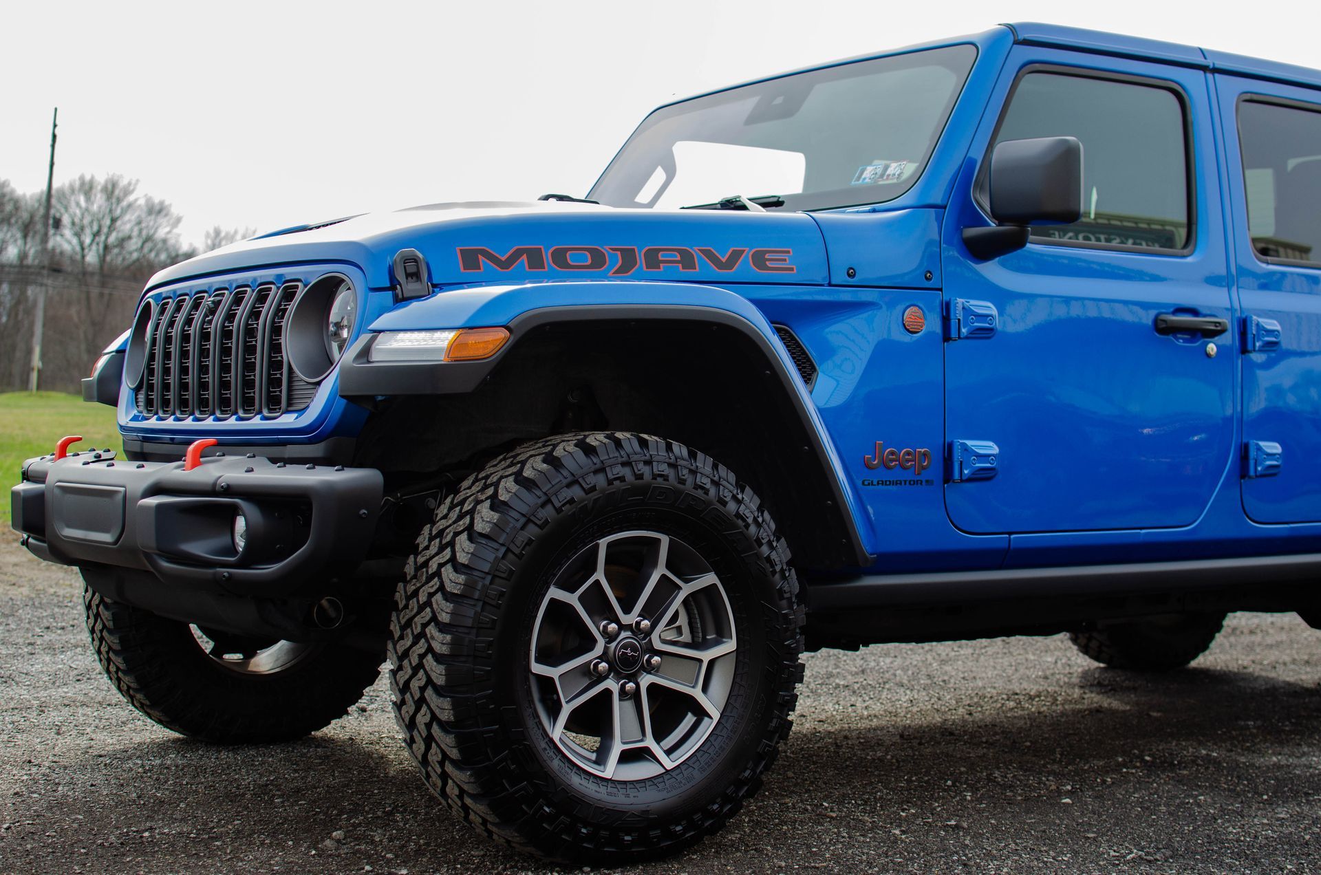 Blue Jeep Wrangler parked outdoors on wet pavement, front-left view.