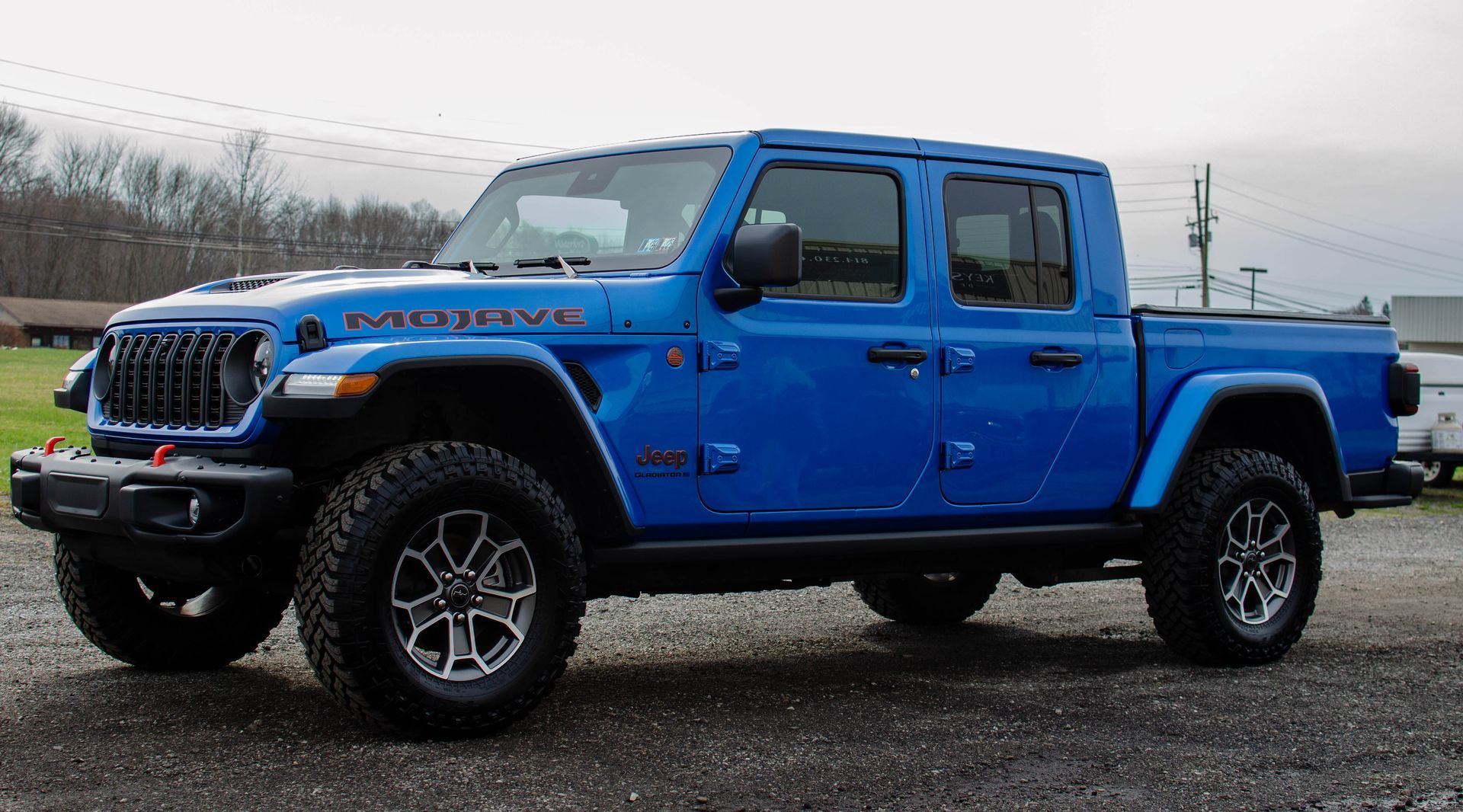 Bright blue lifted Jeep Gladiator pickup parked on gravel under an overcast sky