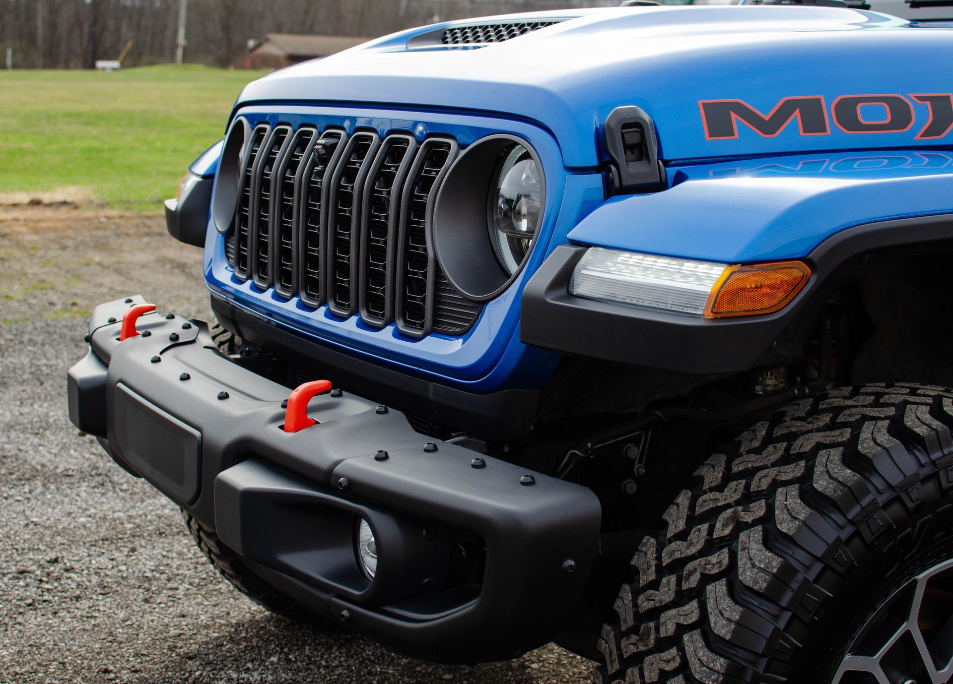 Blue off-road Jeep front end with black grille and bumper, shown on a grassy outdoor trail.