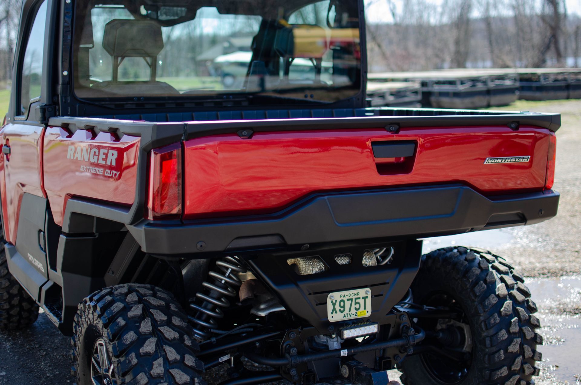 Red utility ATV with open cargo bed and large off-road tires on a snowy outdoor trail.