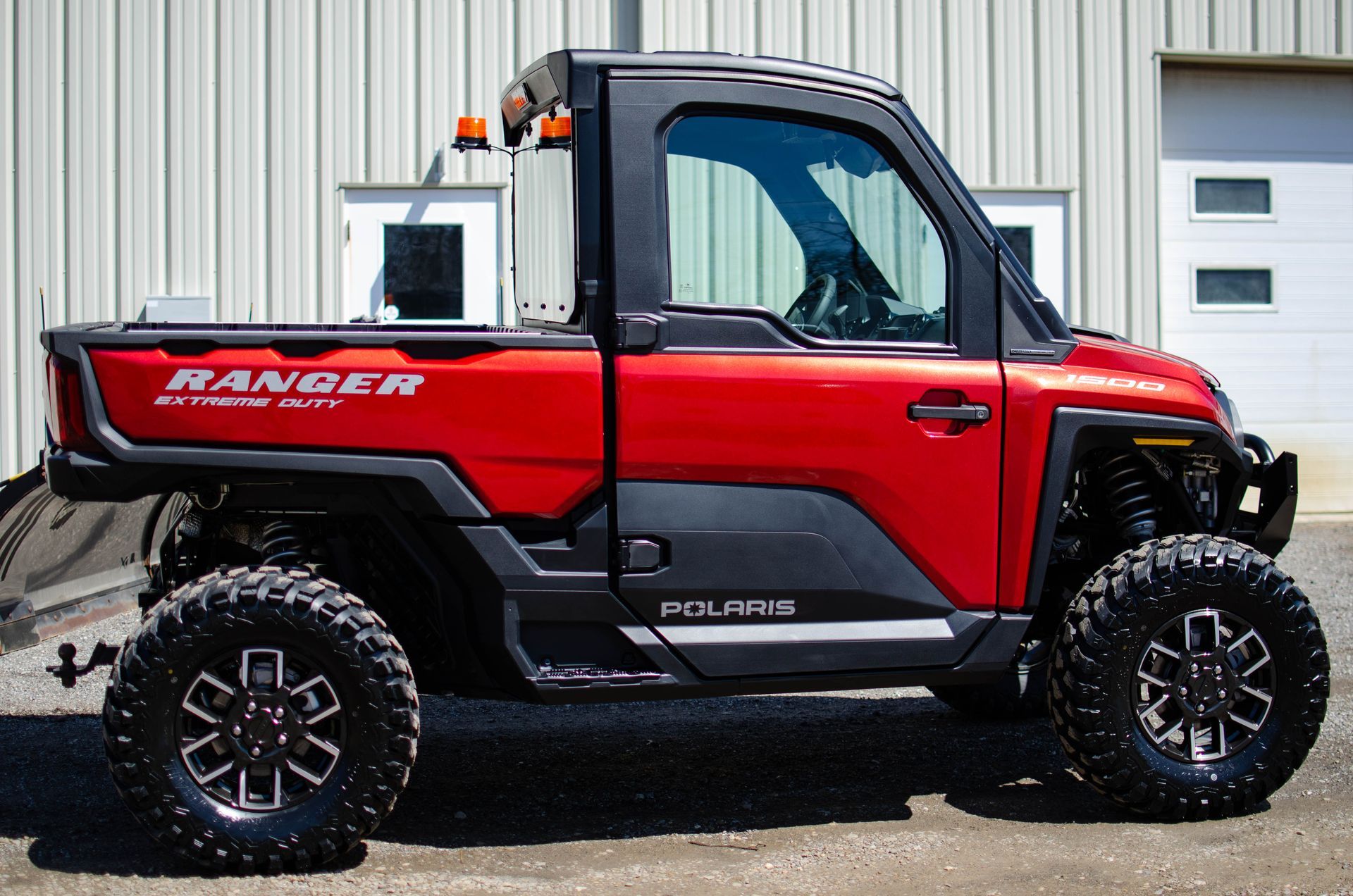 Red Ford Ranger pickup truck with large off-road tires parked beside a building.