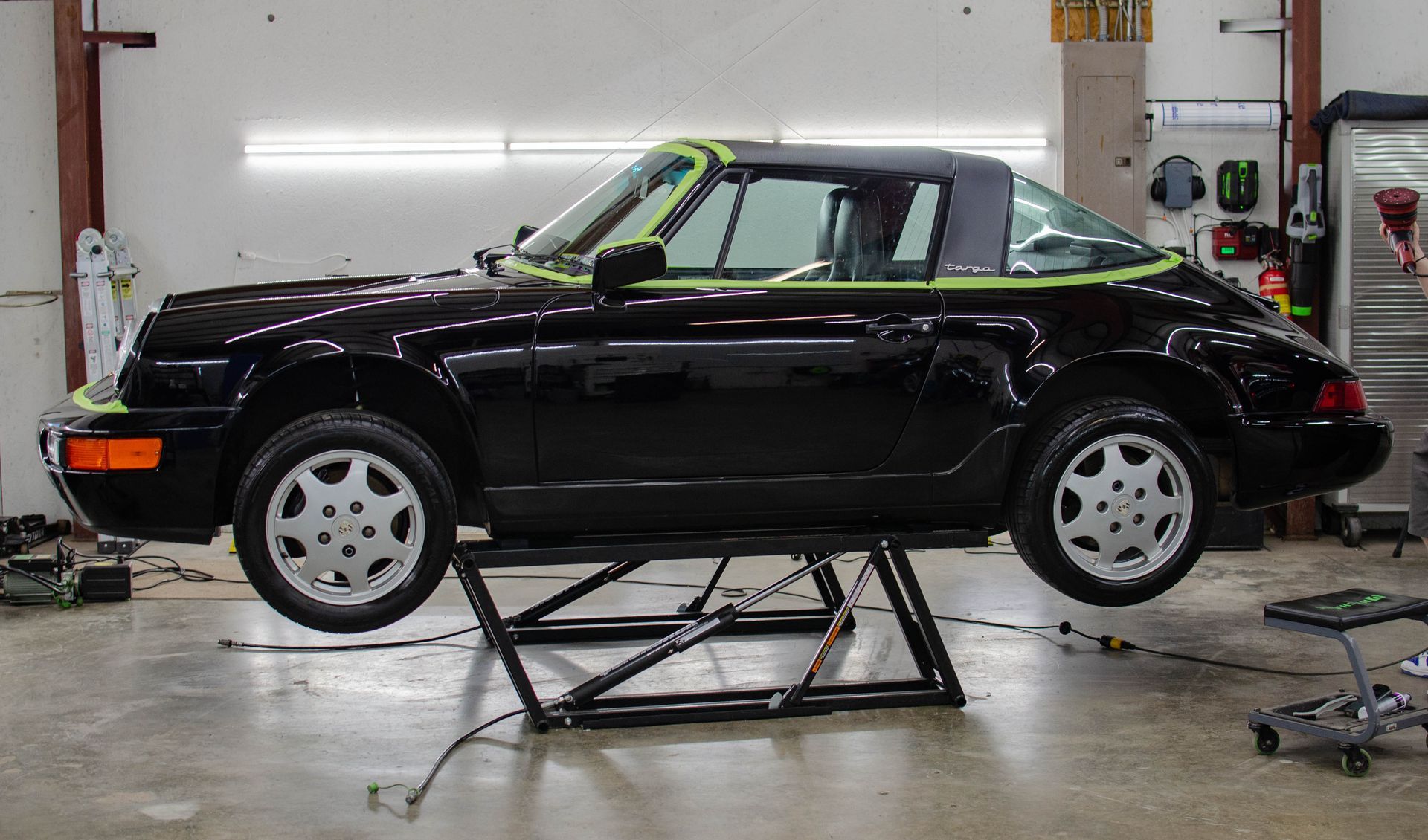 Black sports car on a lift in a garage, side view with white wheels.