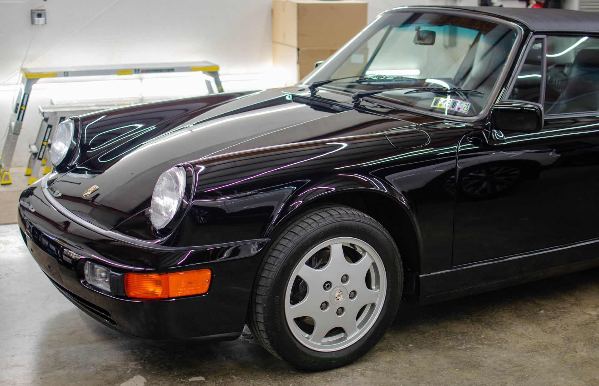 Black sports coupe parked in a garage, front-left view, with silver wheels and amber side marker lights