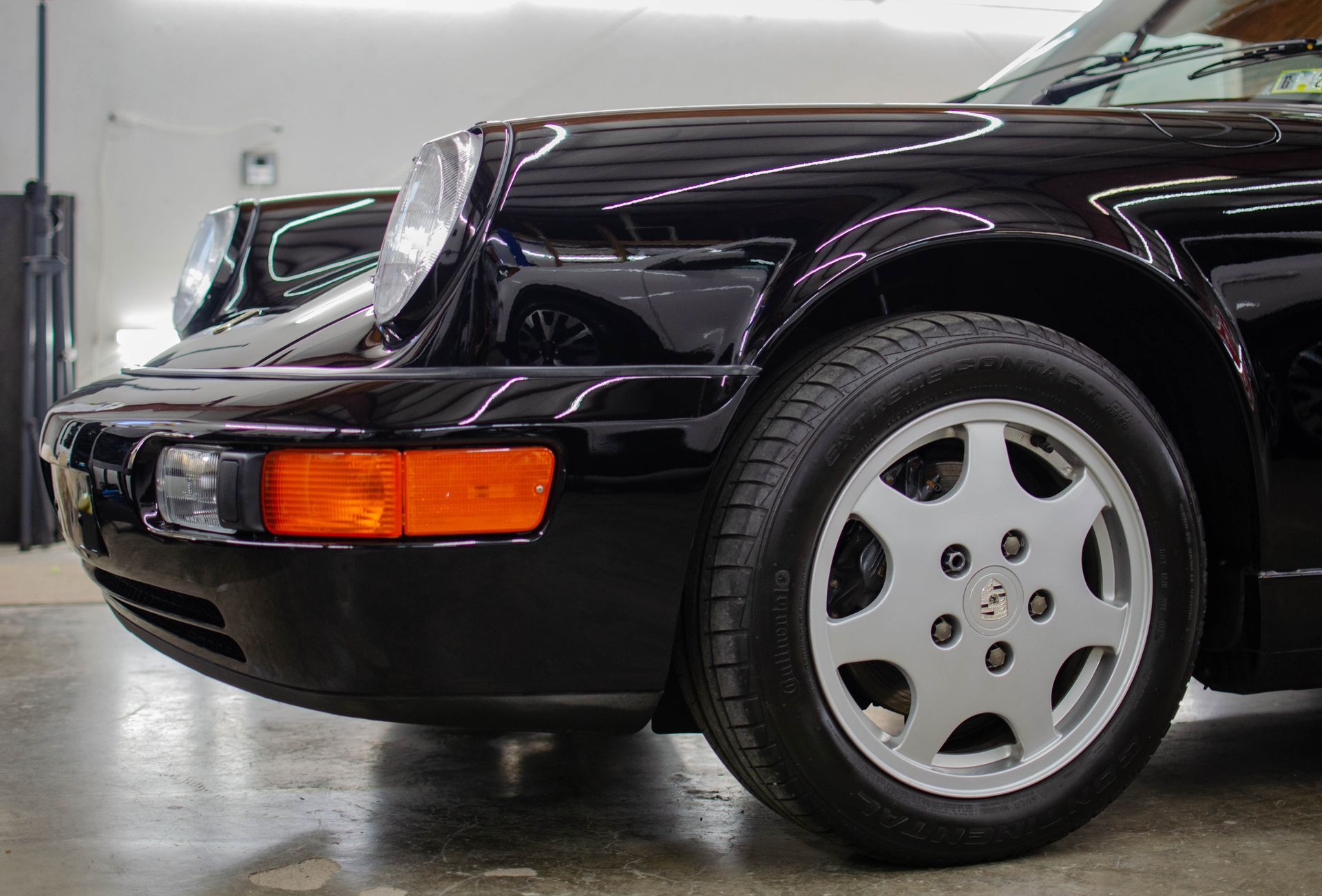 Black sports car front quarter view with orange side marker and silver wheel in a garage.
