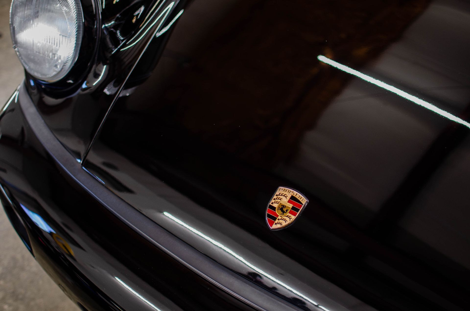 Close-up of a black Porsche hood with the gold-and-red Porsche crest