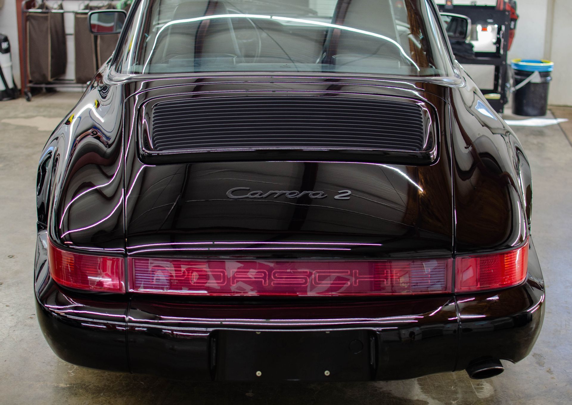 Rear view of a black Porsche 911 Carrera 2 in a garage, with red taillight bar and reflective finish