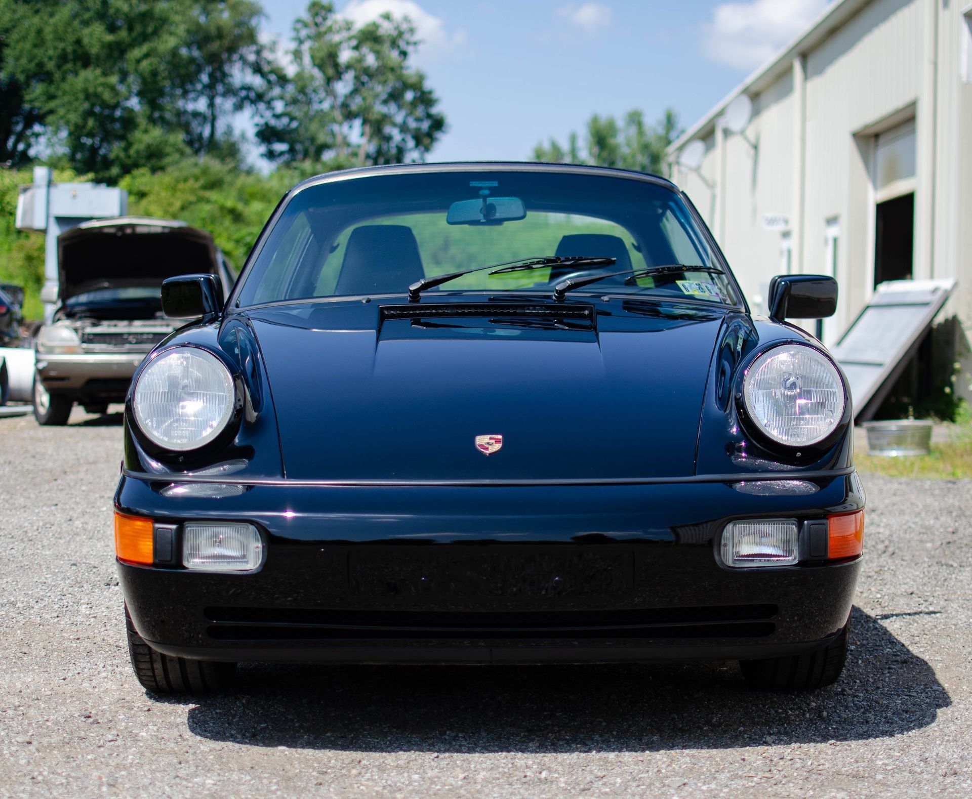 Front view of a dark blue Porsche 911 parked outdoors on a sunny day.