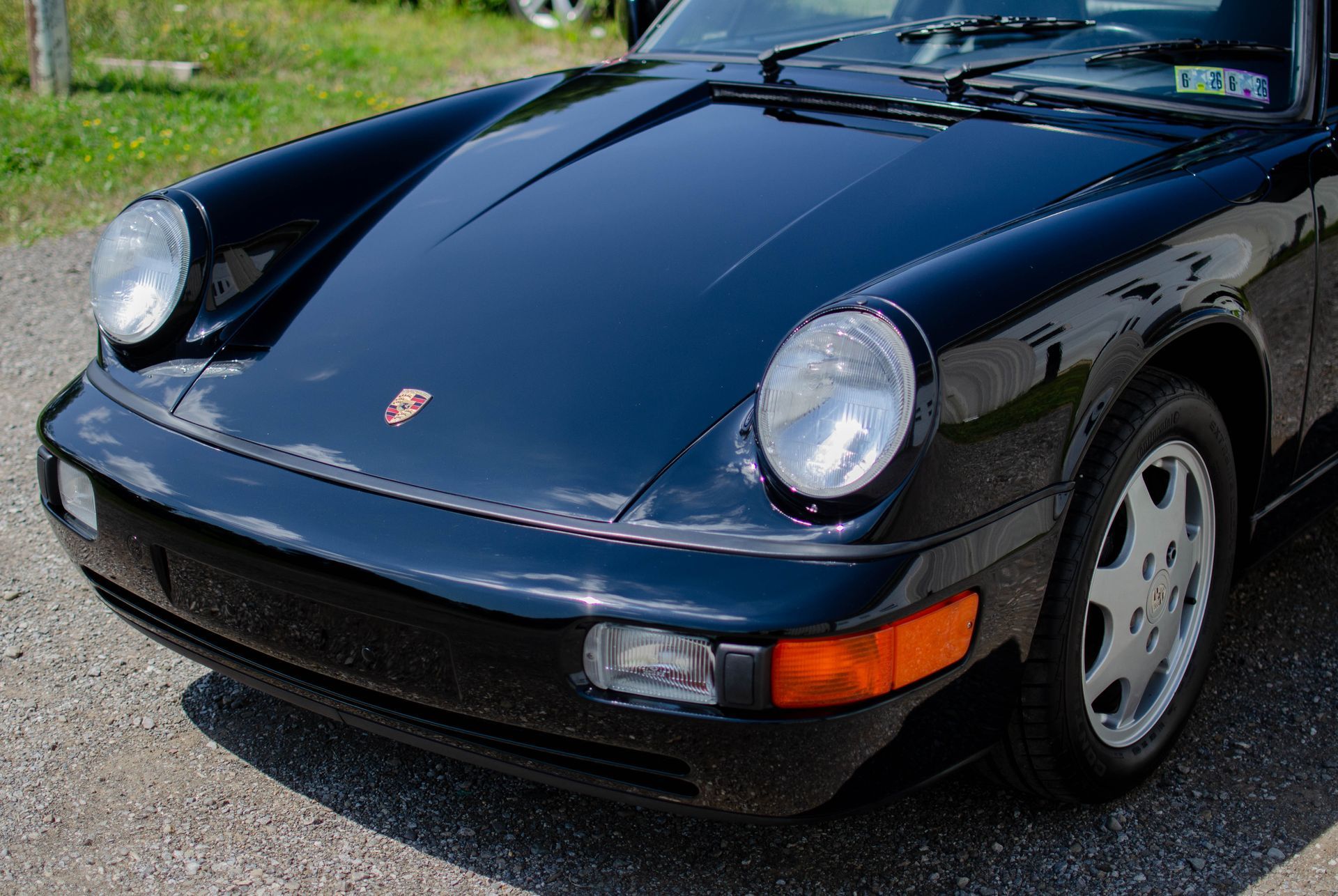 Black Porsche 911 parked outdoors on a gravel surface, front-left view