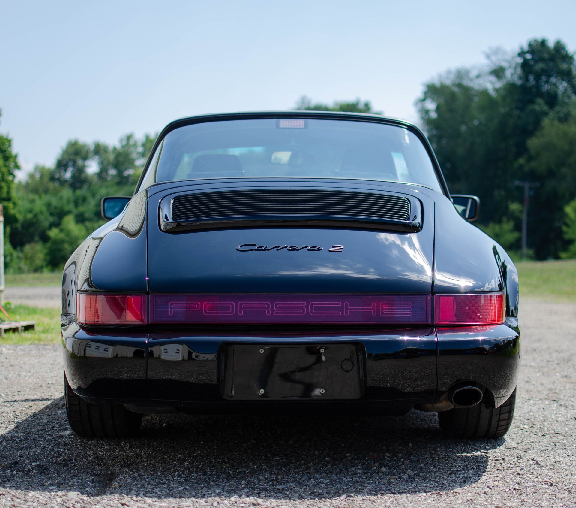 Rear view of a black Porsche 911 with a pink taillight bar on a gravel road outdoors