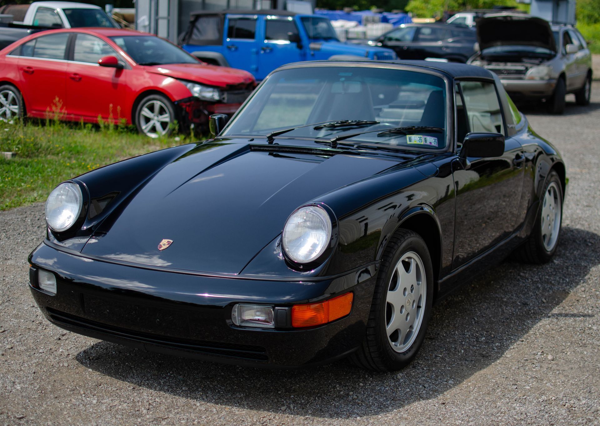 Black Porsche 911 convertible parked outdoors at a car show, with other cars in the background