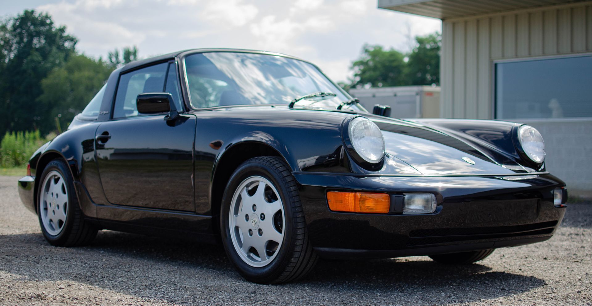 Black Porsche 911 parked outdoors on pavement, front-left view