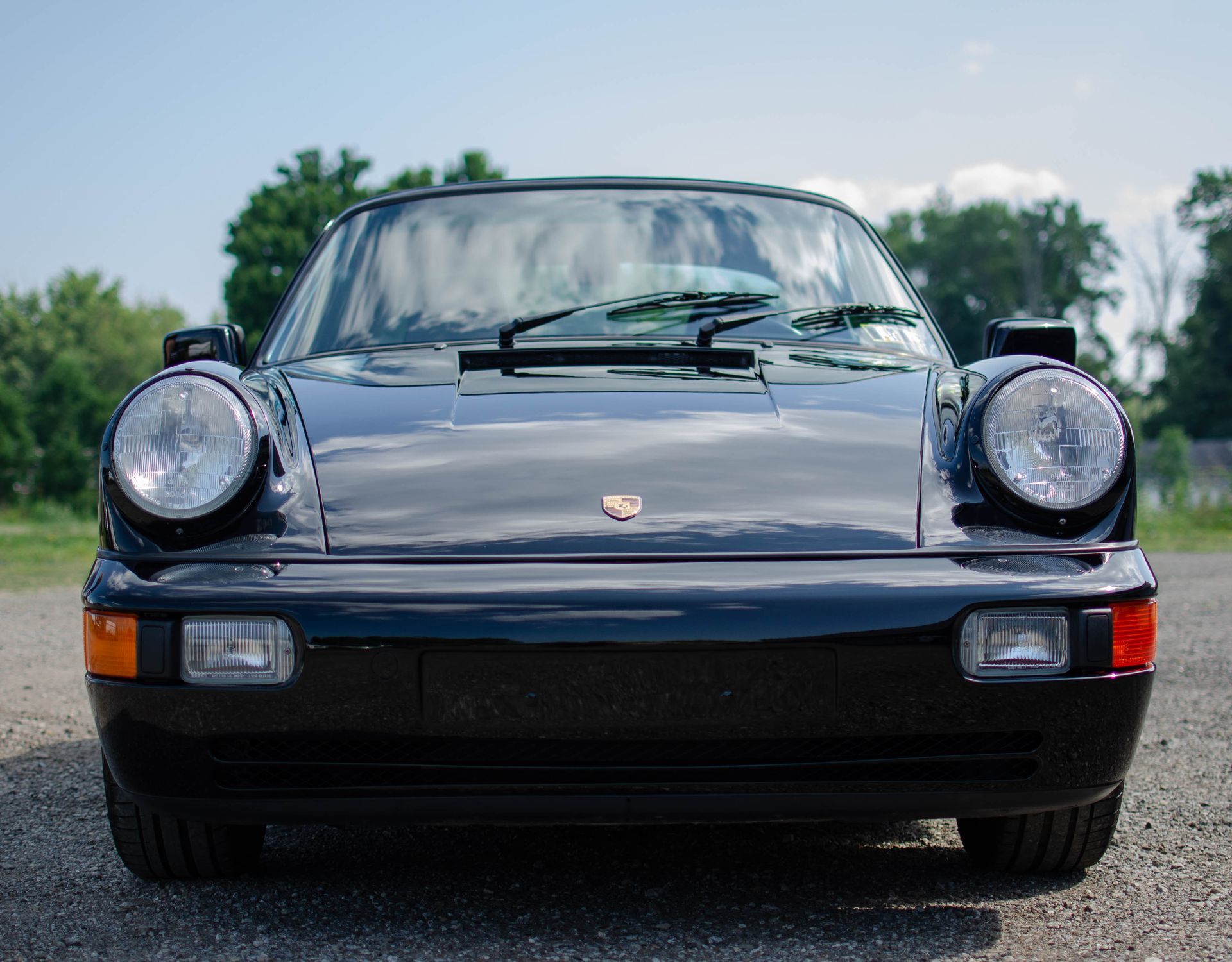 Front view of a black classic Porsche 911 parked on a road with trees in the background