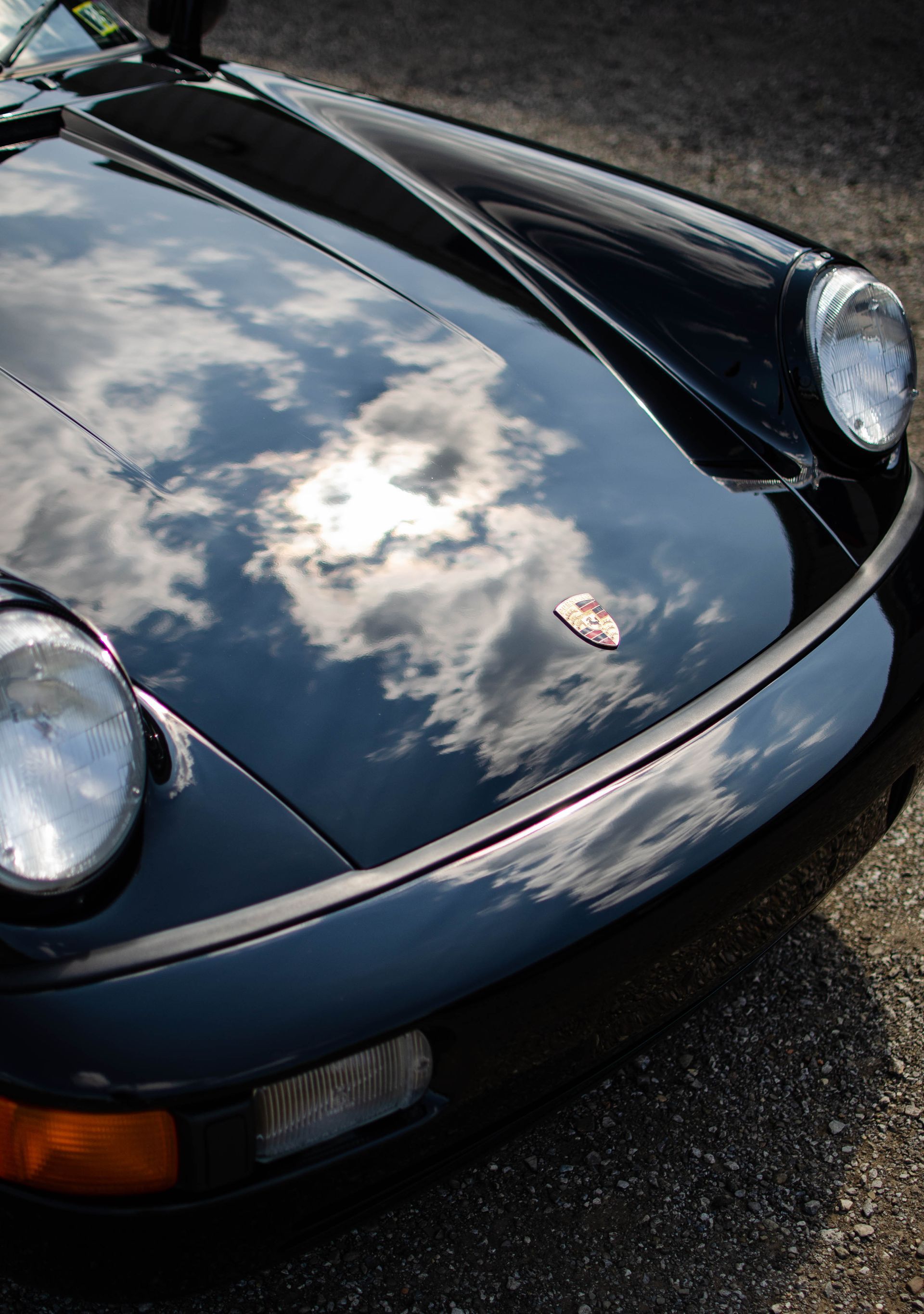 Front view of a dark blue sports car with pop-up headlights reflecting clouds on its hood