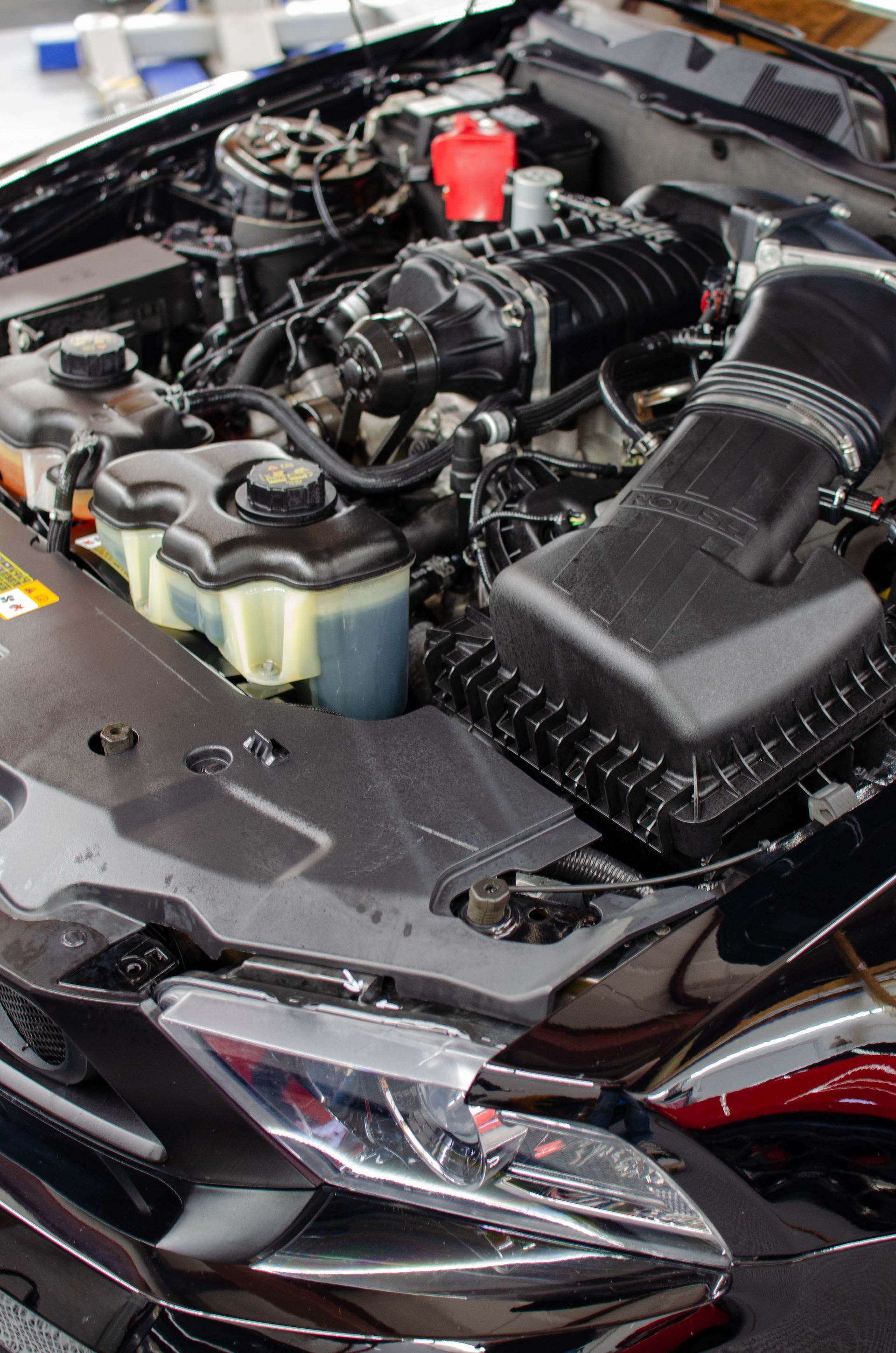 Car engine bay with exposed components, black intake box, and red battery terminal.