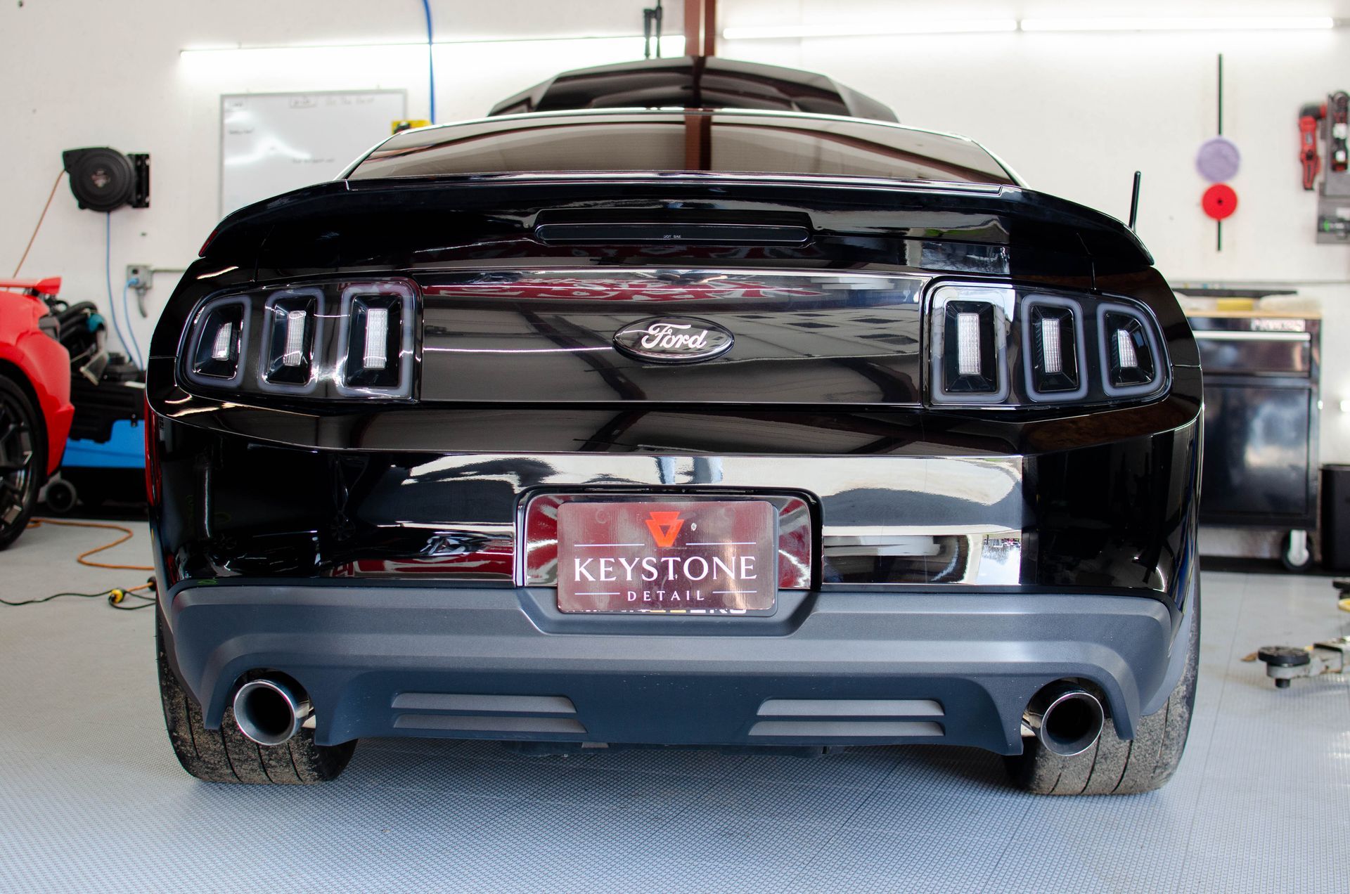 Rear view of a black Ford Mustang in a garage, with triple taillights and Keystone plate frame.