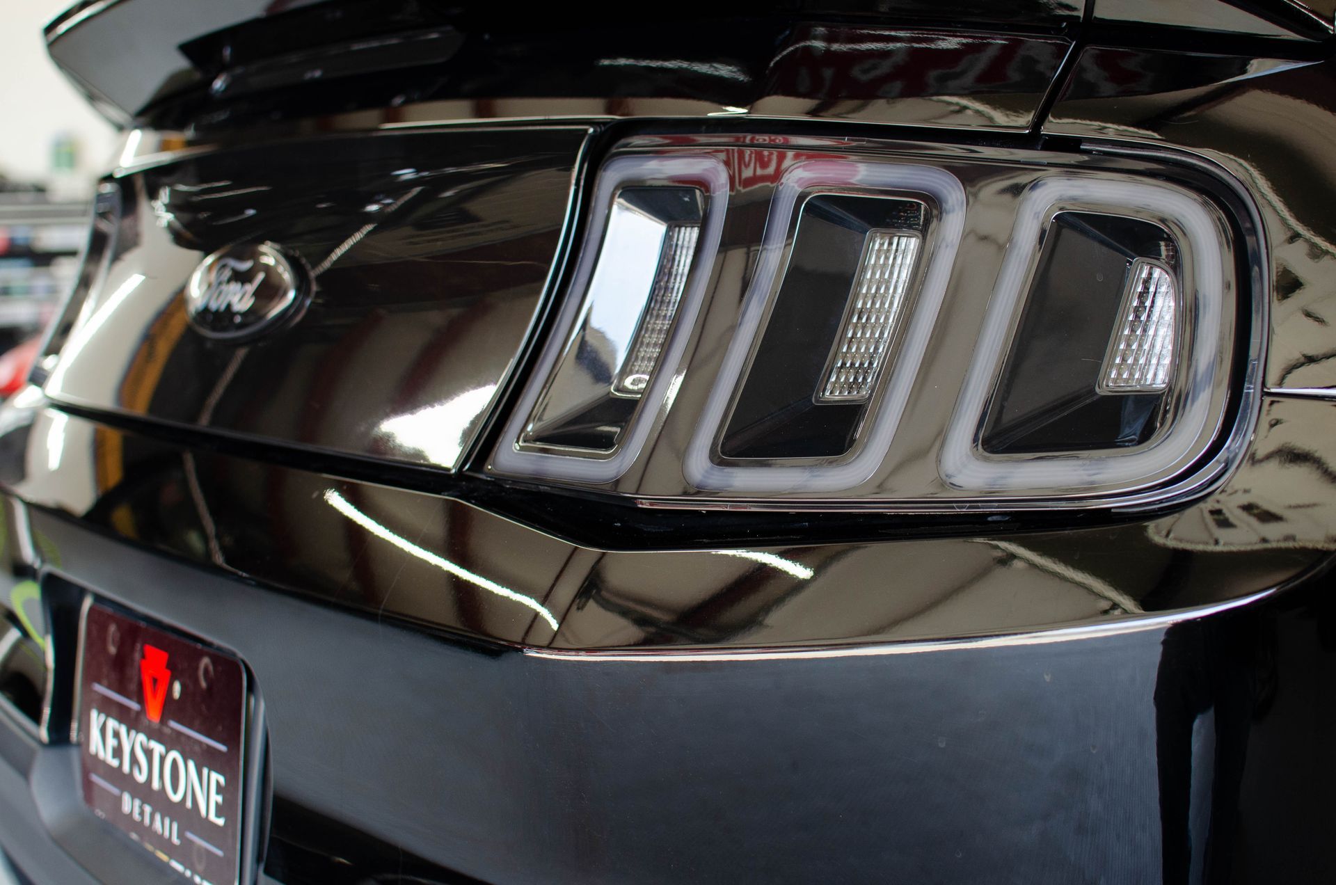 Close-up of a glossy black car’s rear taillights and trunk badge at a dealership