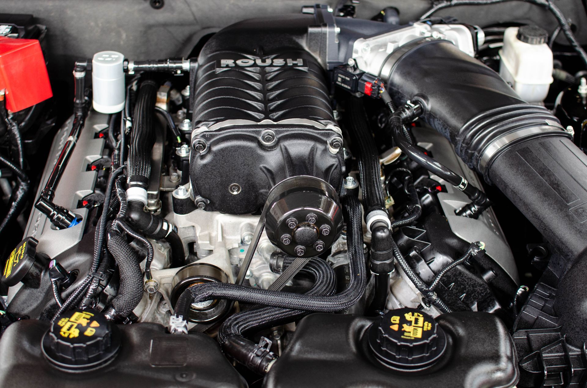 Car engine bay with a black supercharger and chrome intake components.
