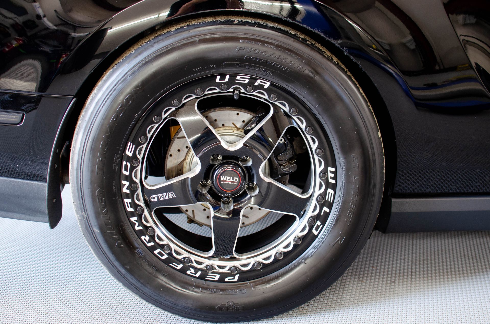 Close-up of a black car wheel with chrome five-spoke rim and white-letter tire sidewall.