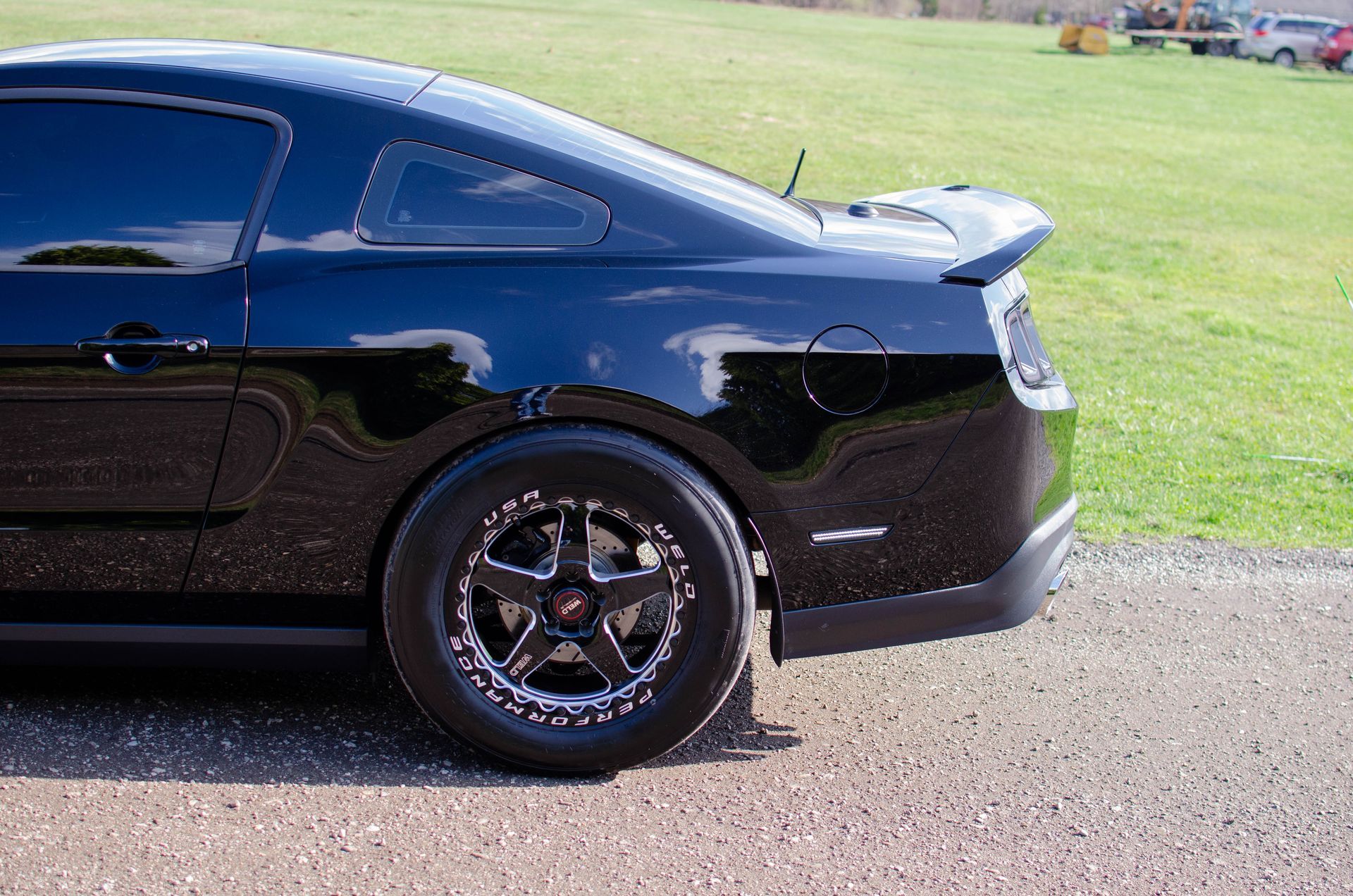 Black sports car parked on gravel beside a grassy field