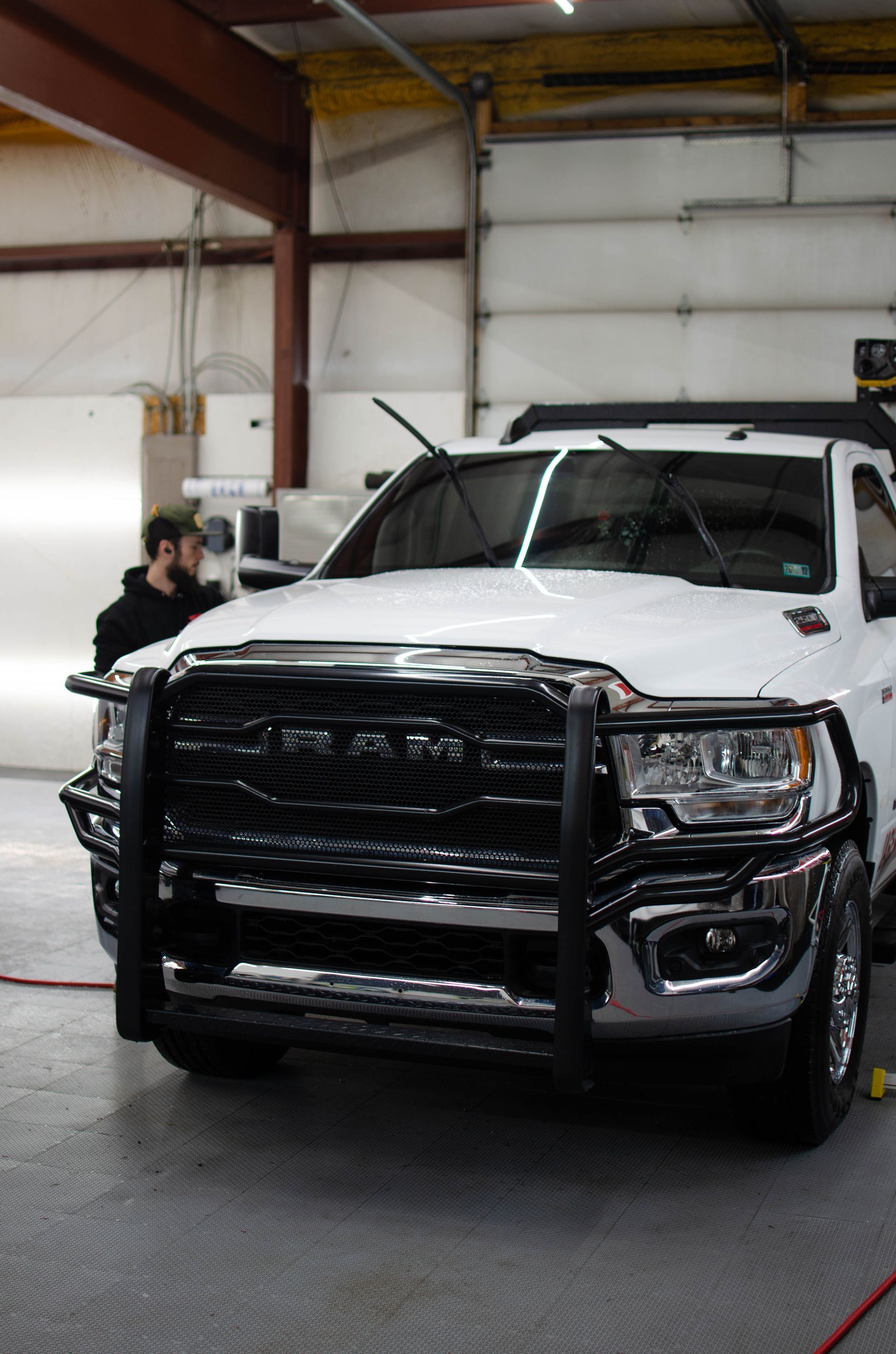 White pickup truck with a black grille guard in a warehouse, with a person working beside it