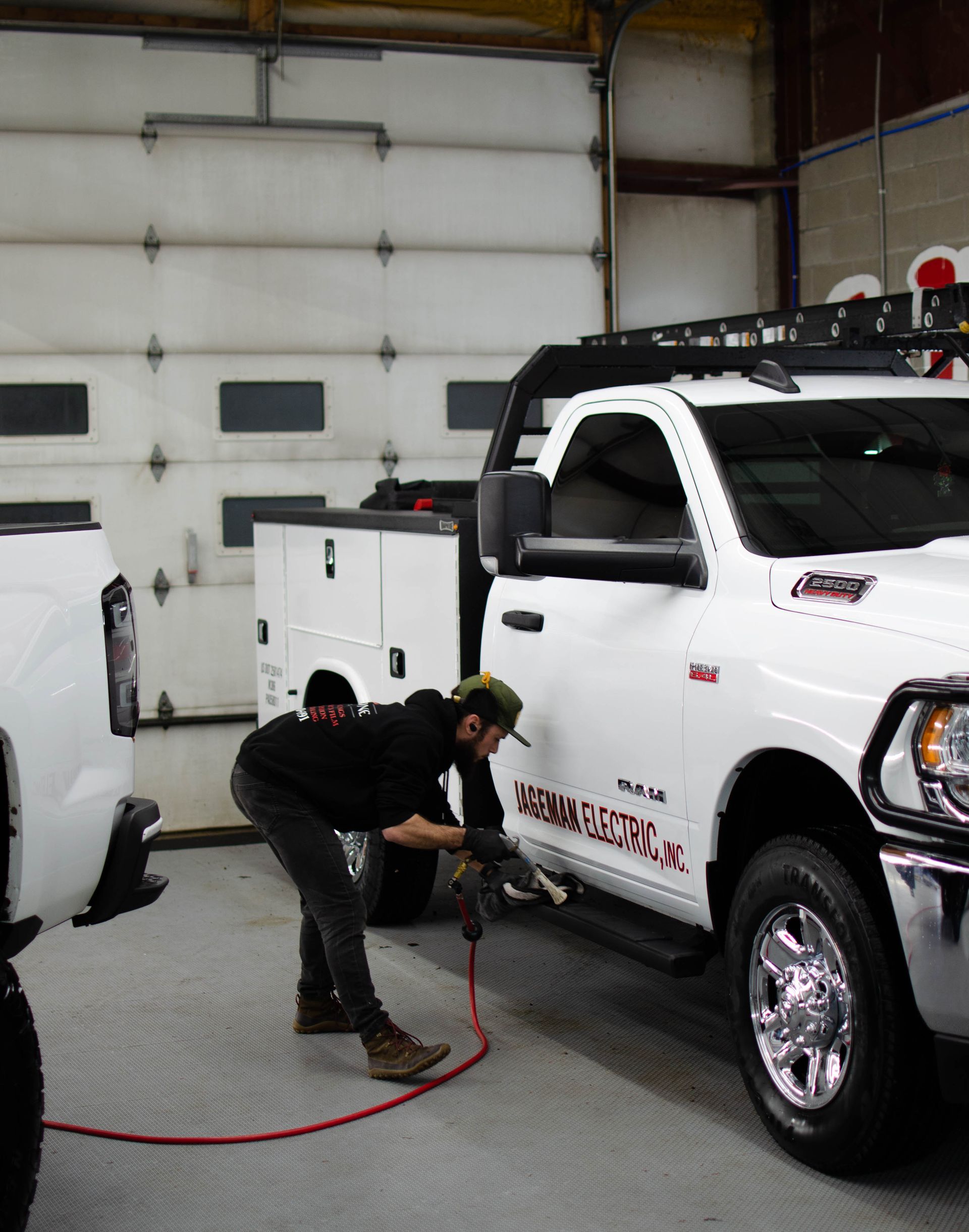Technician polishing a white pickup truck in a garage with a red hose on the floor