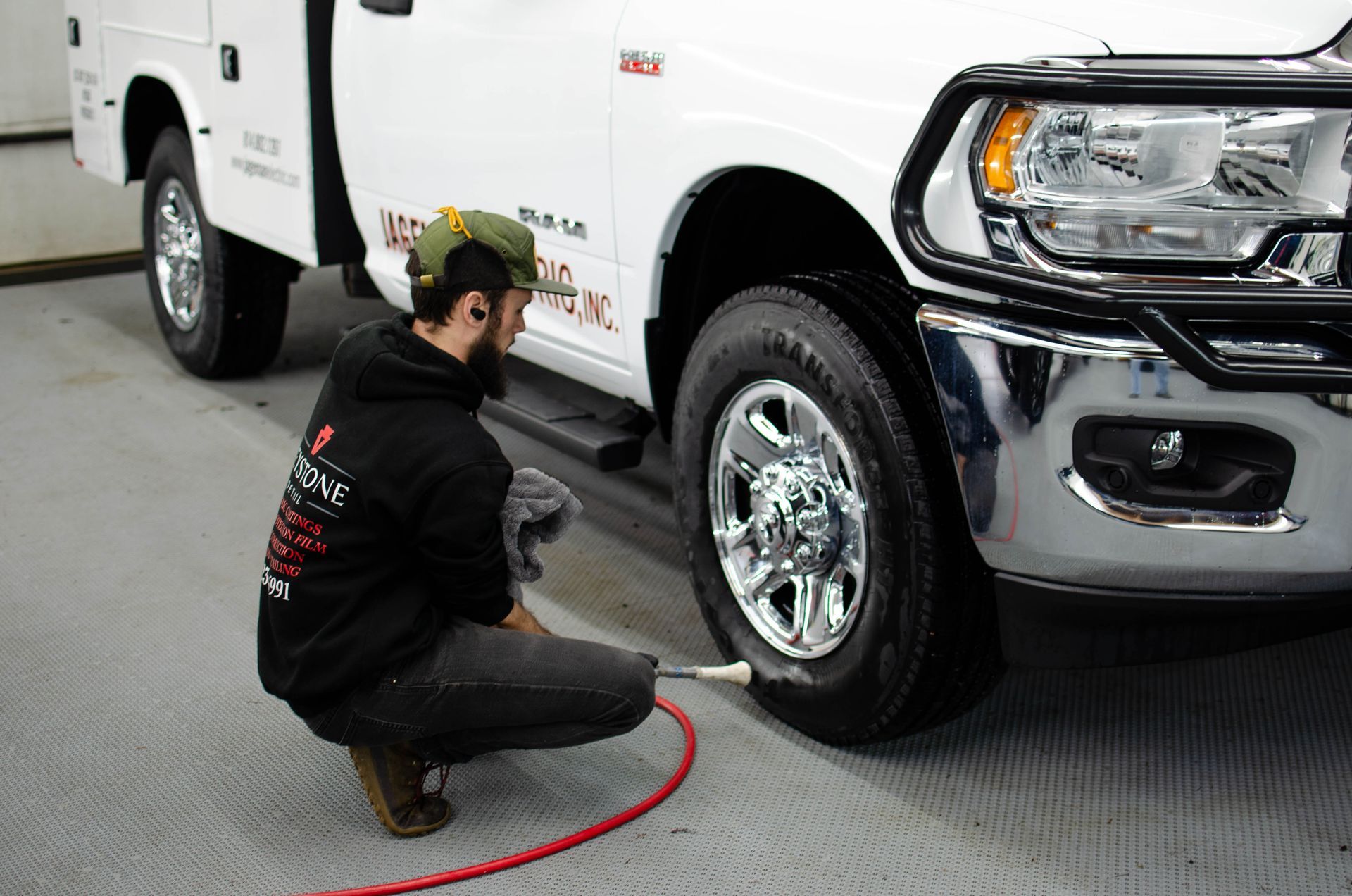 Mechanic kneeling by a white pickup truck, inspecting the front wheel in a garage.