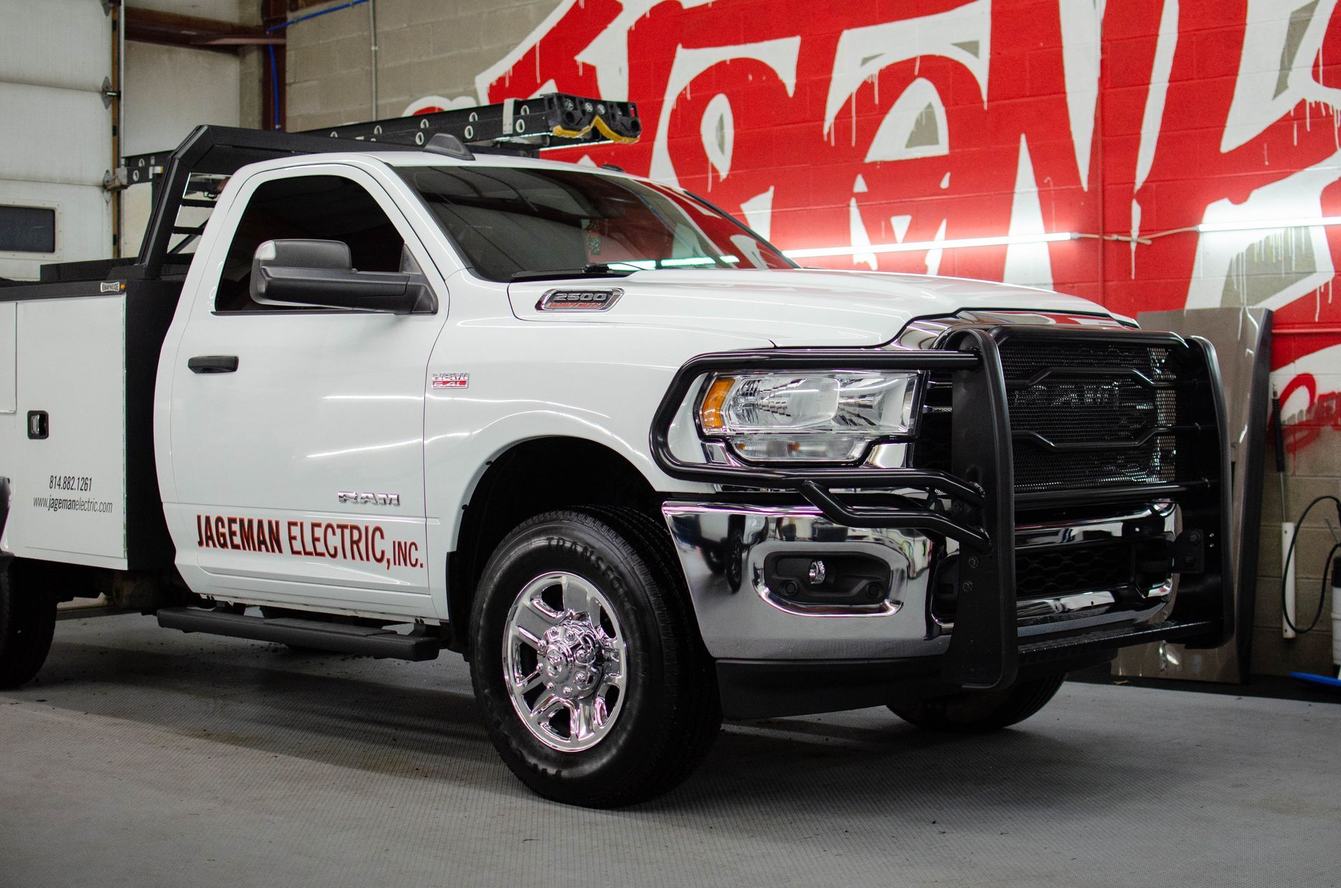 White tow truck with black grille parked indoors in front of a red wall mural