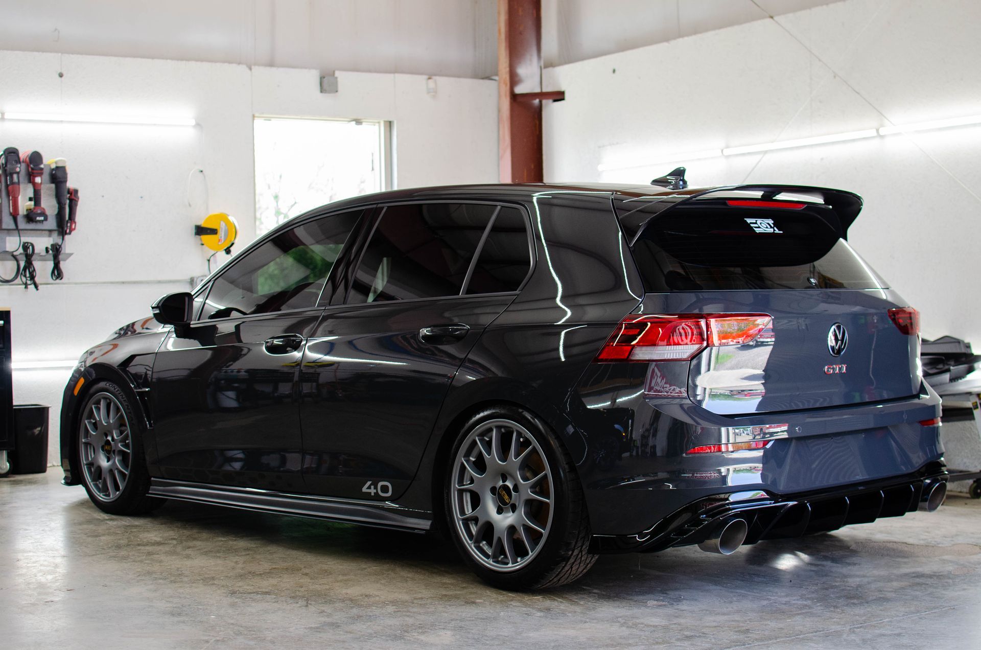 Black modified hatchback parked in a garage, side view with tinted windows and aftermarket wheels
