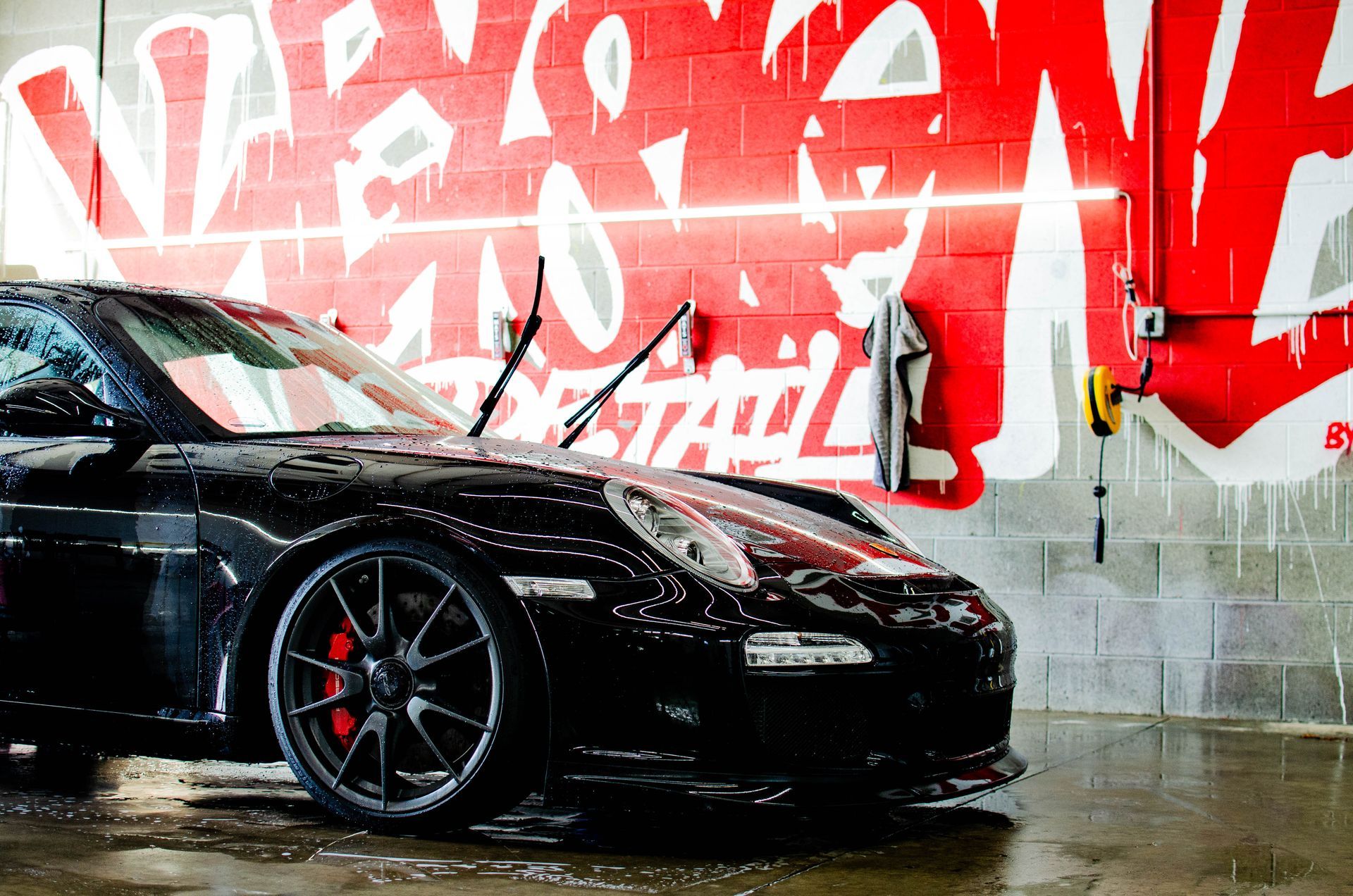 Black sports car in a wet garage, parked before a red graffiti mural