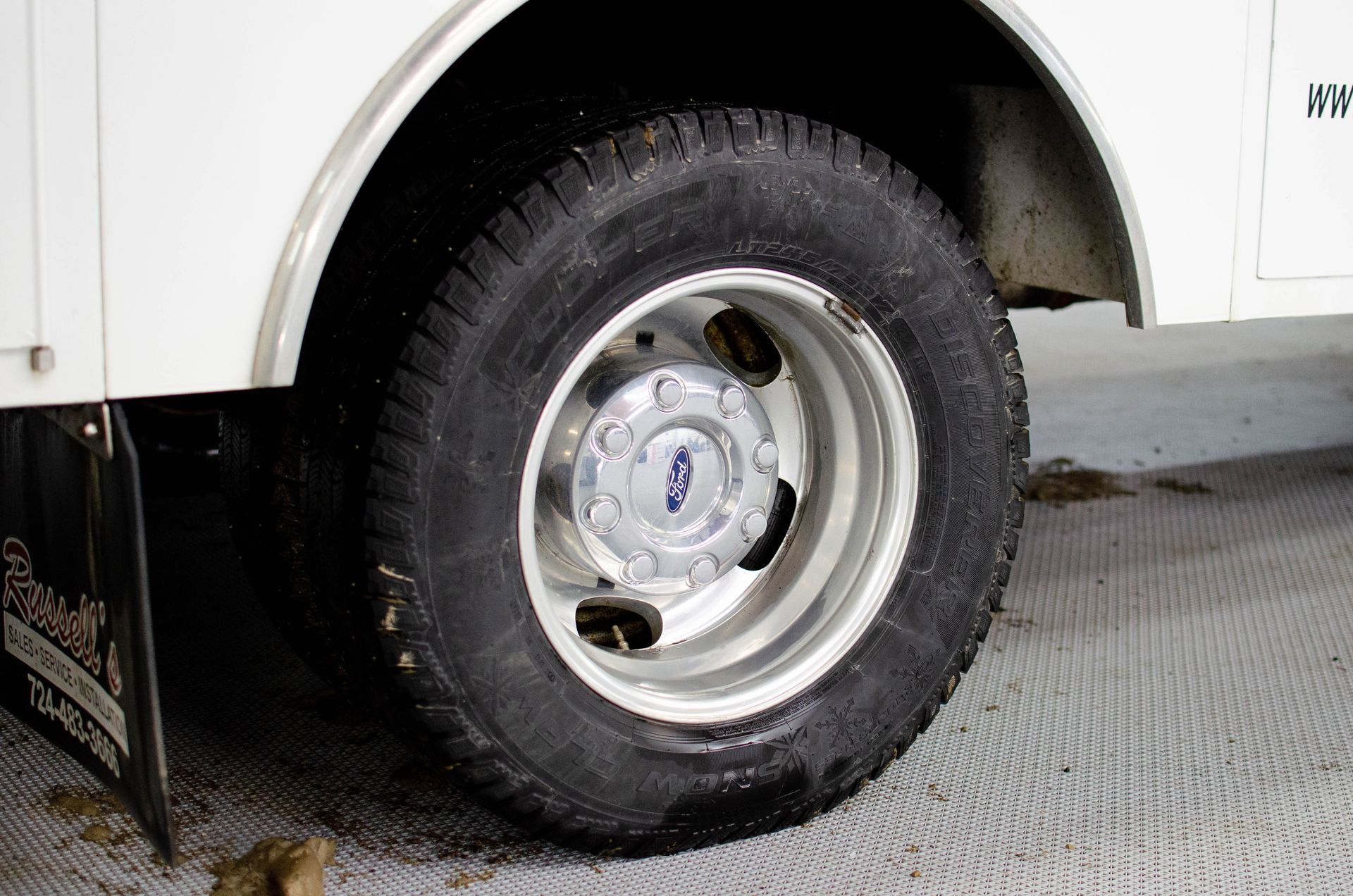 Close-up of a truck’s rear wheel and tire on a textured floor.