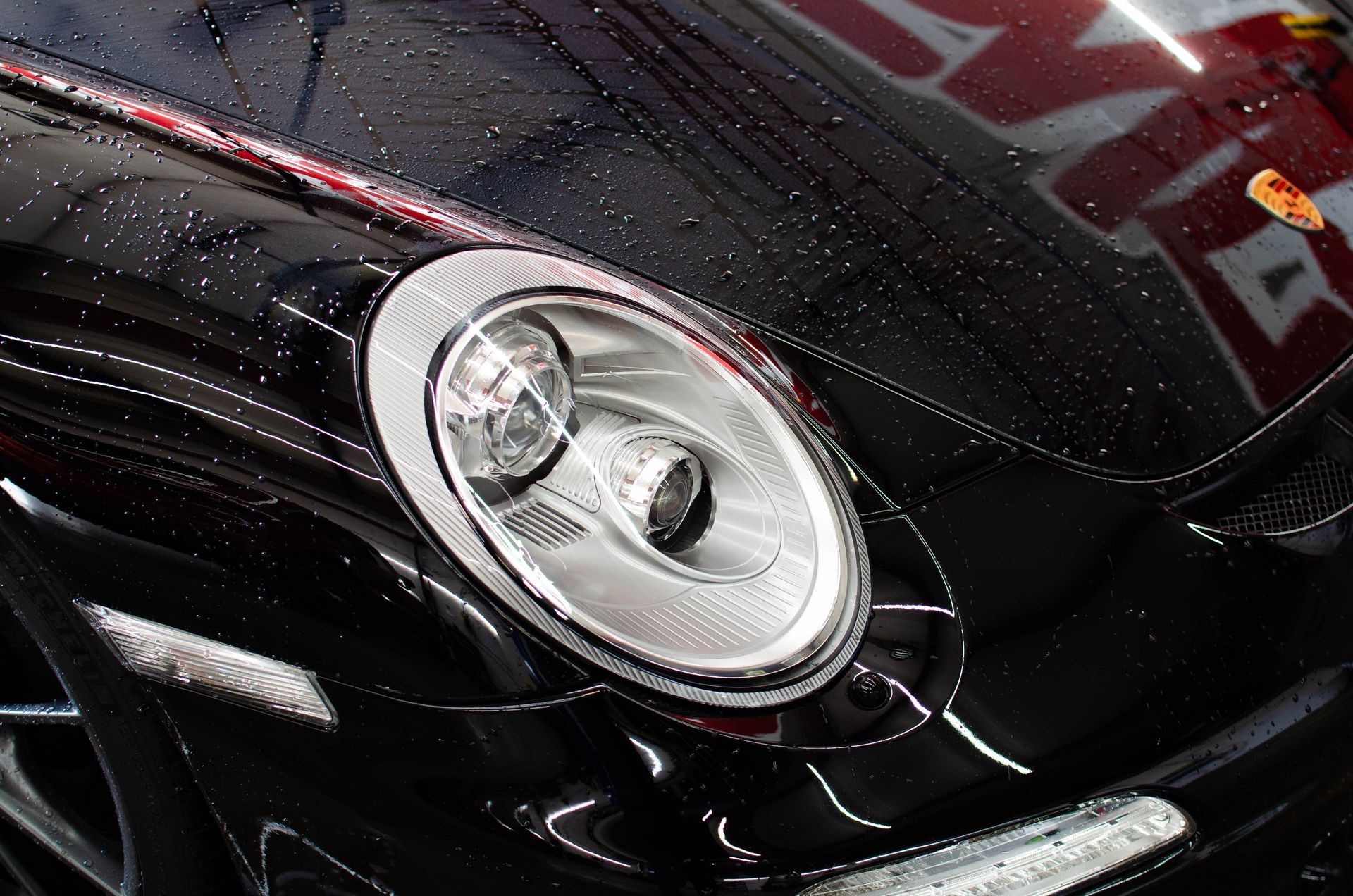 Close-up of a black car’s headlight on a glossy hood with raindrops