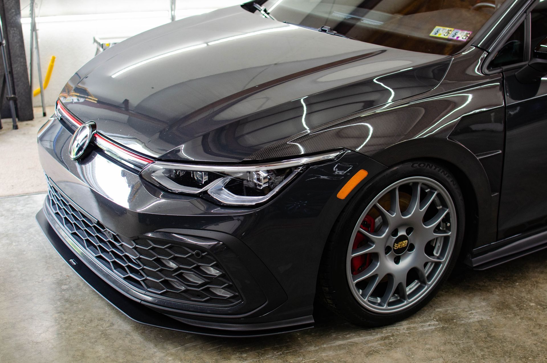 Dark gray sports car with custom wheels parked indoors at a garage.