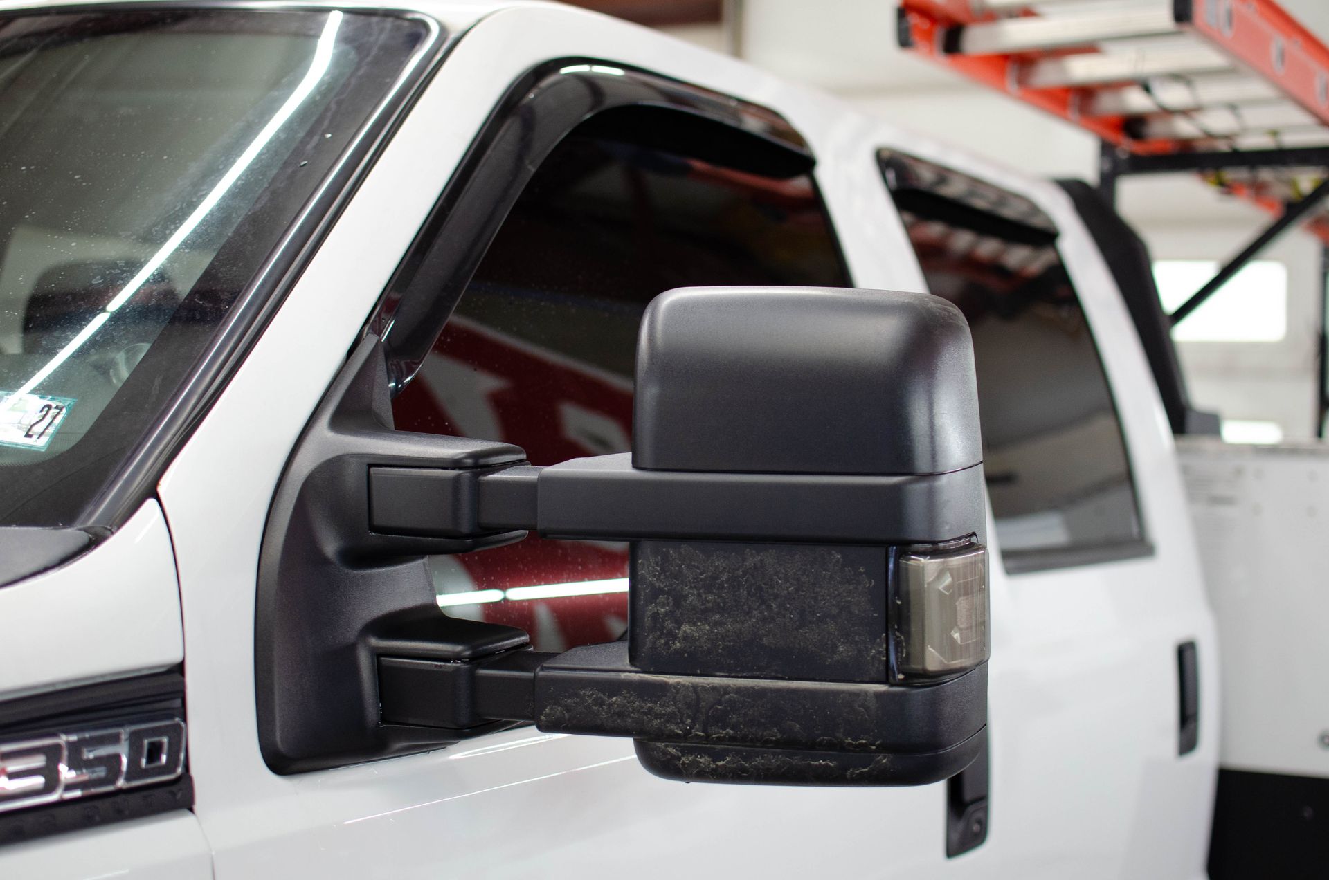 Close-up of a white pickup truck’s black side mirror and door in a garage