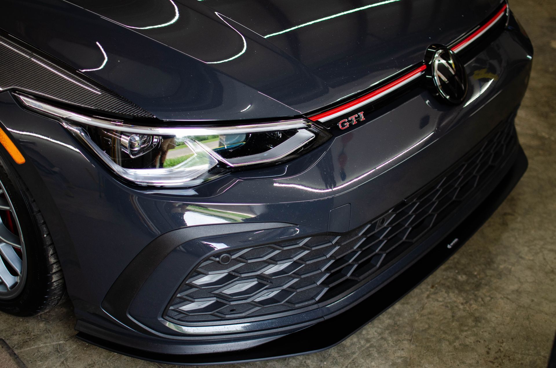 Front view of a dark gray Volkswagen GTI hatchback with red accent stripe in a garage