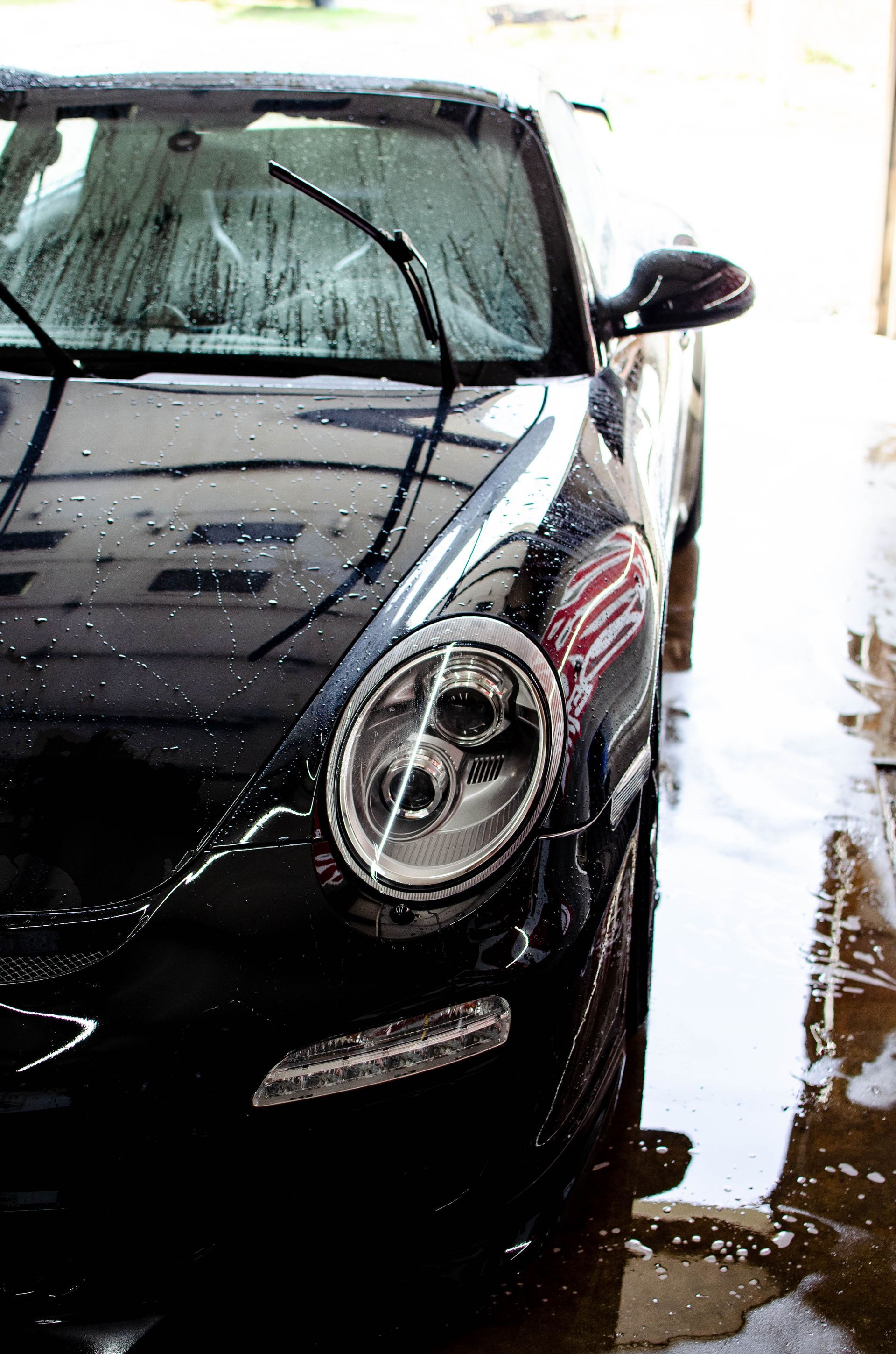 Black car being washed with water and soap suds in a car wash tunnel