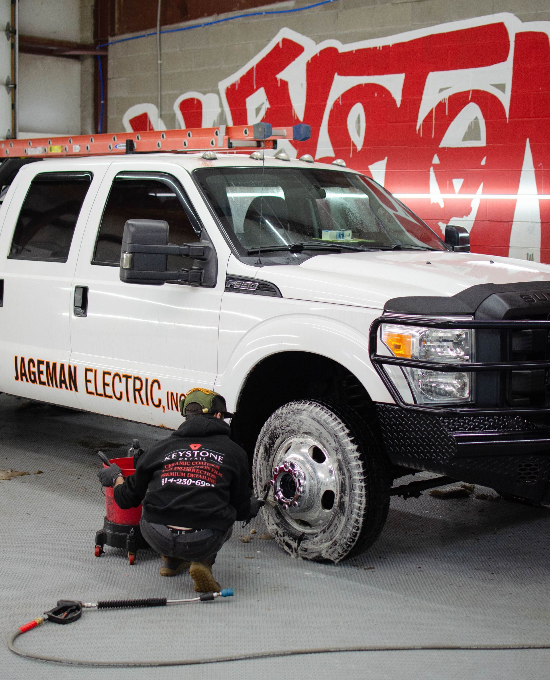 Mechanic working on a white Nissan Electric pickup in a garage with a red graffiti wall.