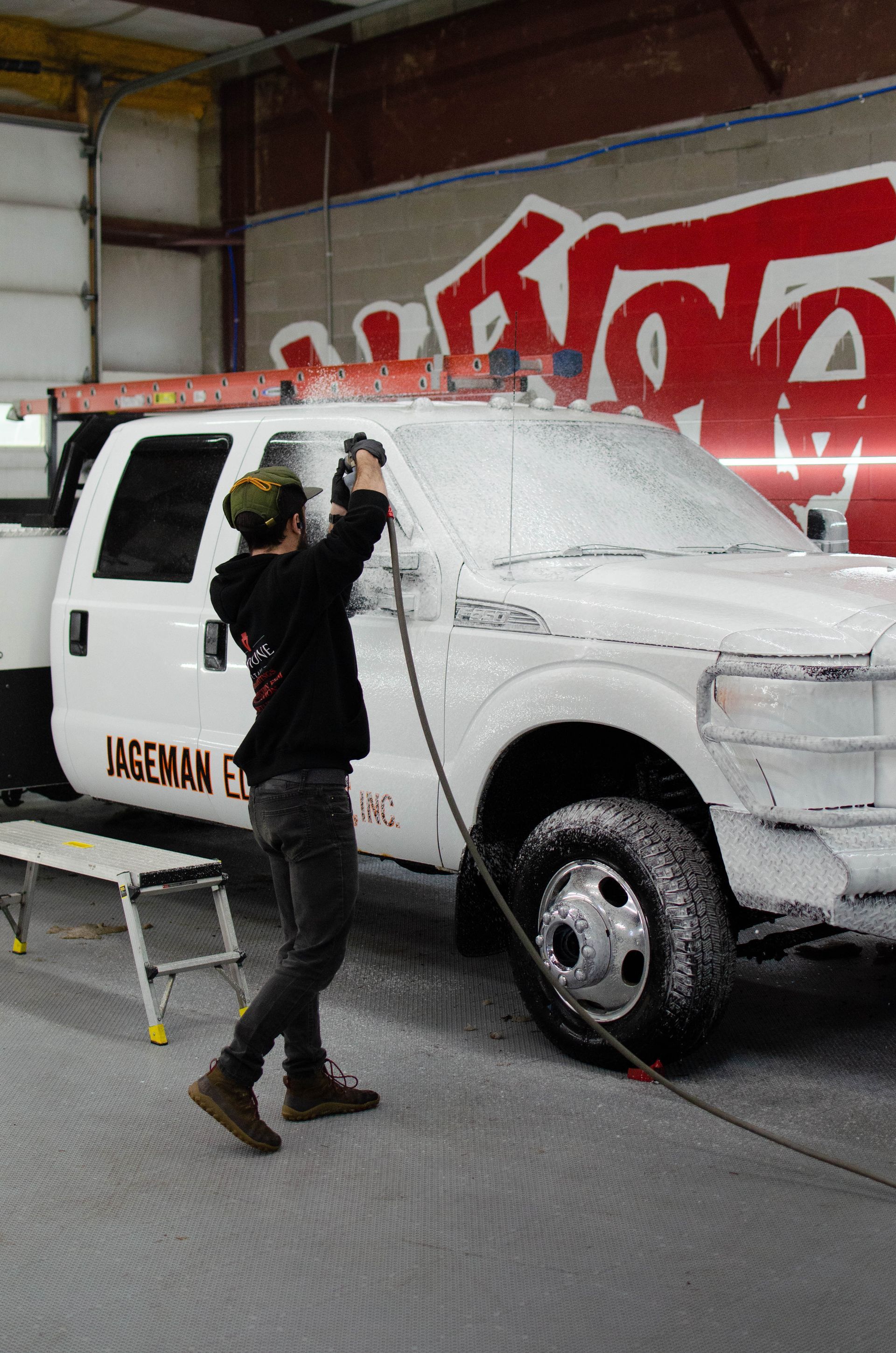 Person spray-paints a white van in a workshop, with red graffiti on the wall behind.