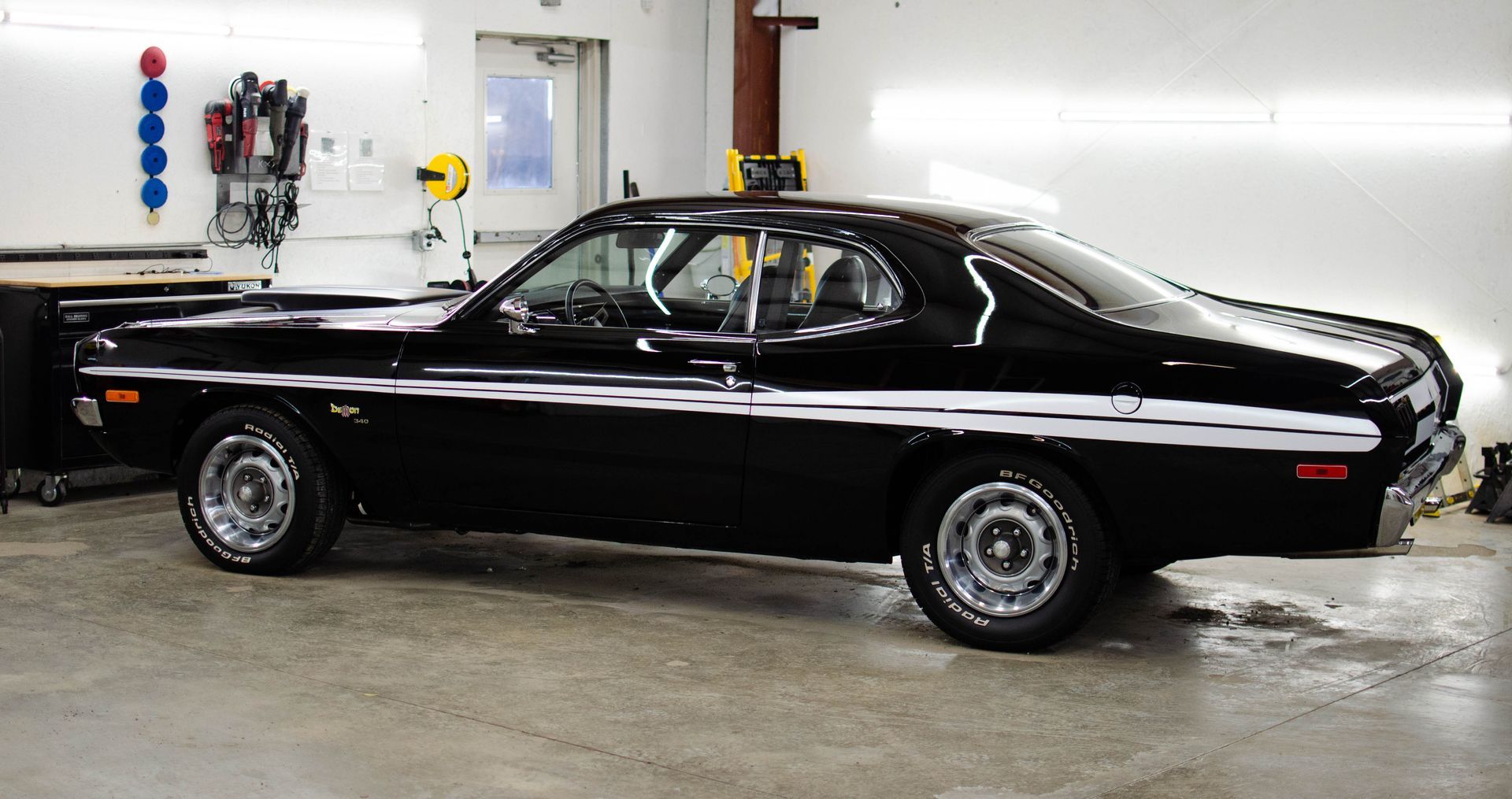 Black classic coupe parked in a garage, side view, with glossy paint and chrome trim