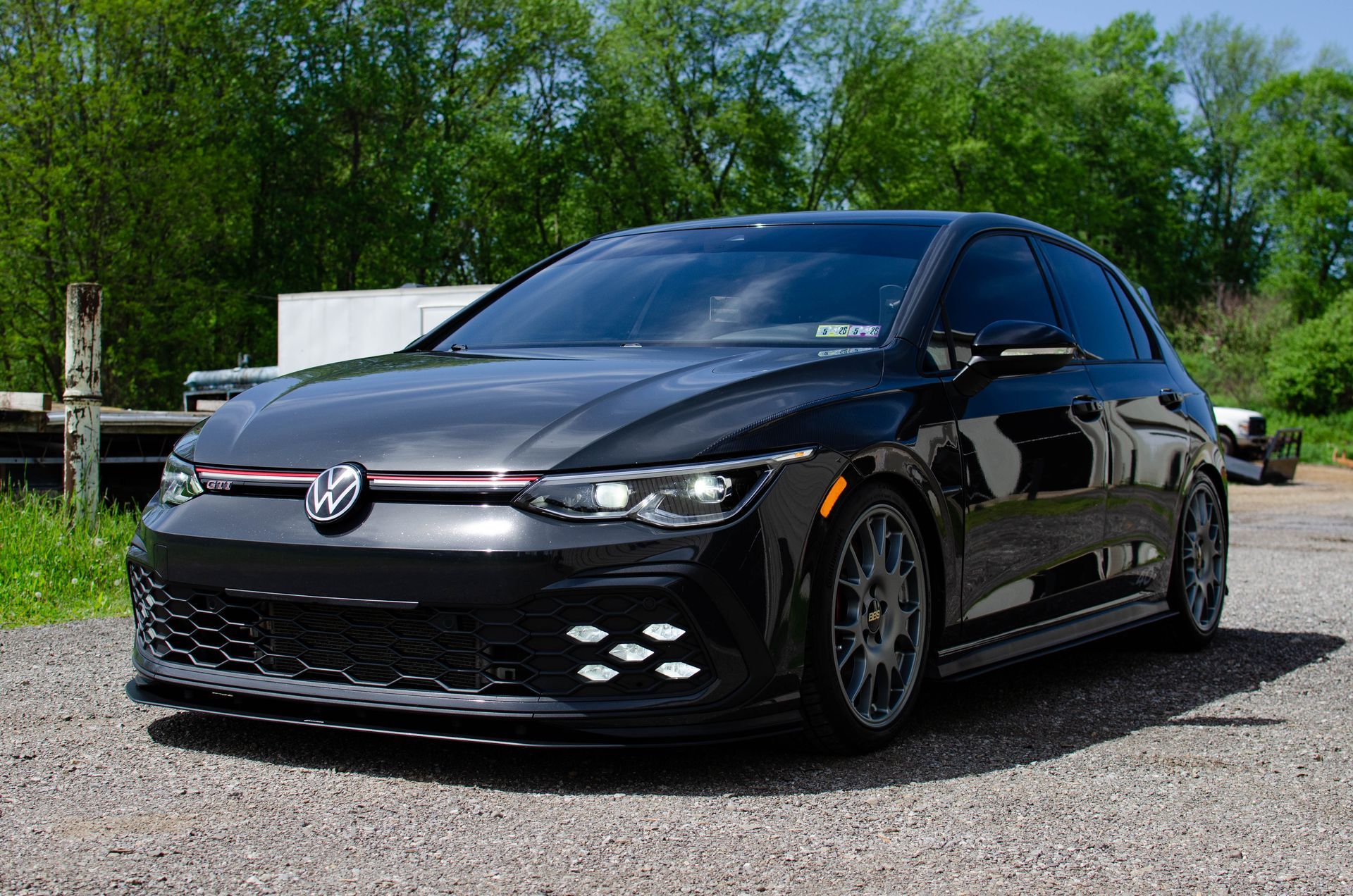 Black Volkswagen hatchback parked on gravel with trees in the background