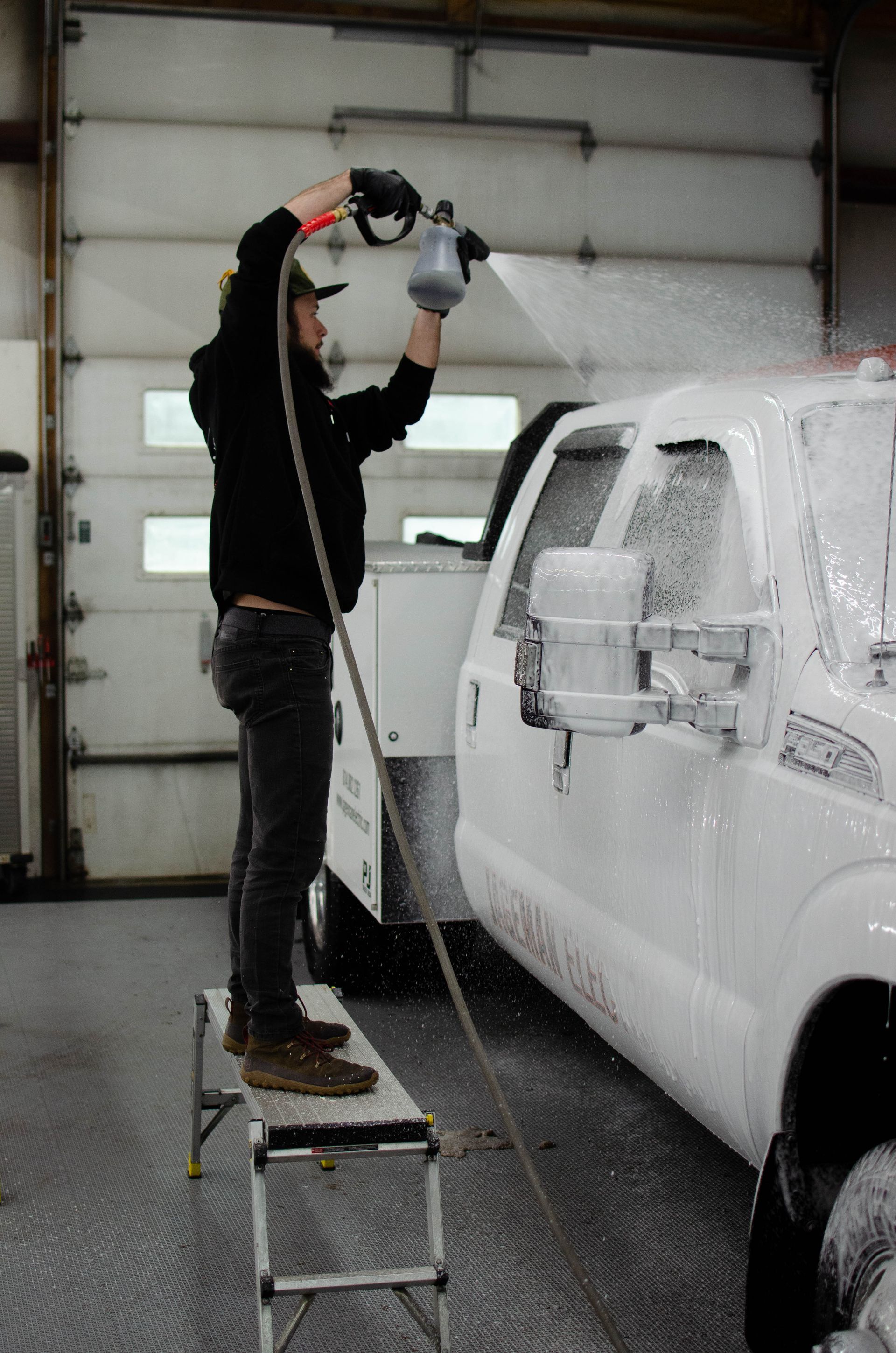 Person on a step stool spray-painting a white pickup truck in a garage