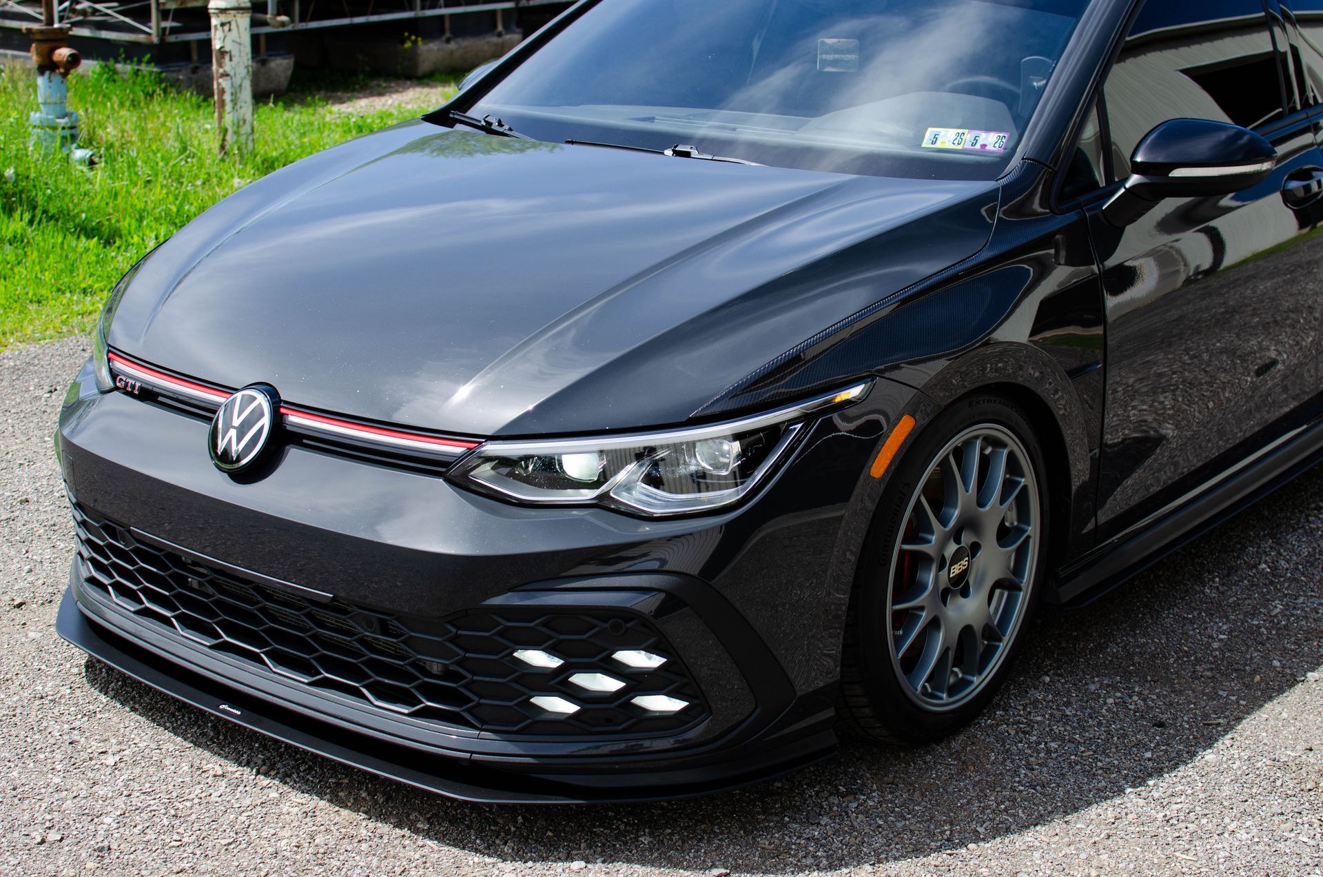 Black Volkswagen hatchback parked on a roadside, front view with red grille stripe and alloy wheels
