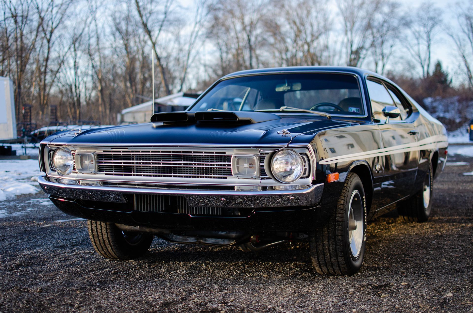 Classic black muscle car parked on a snowy roadside with a hood scoop and chrome grille