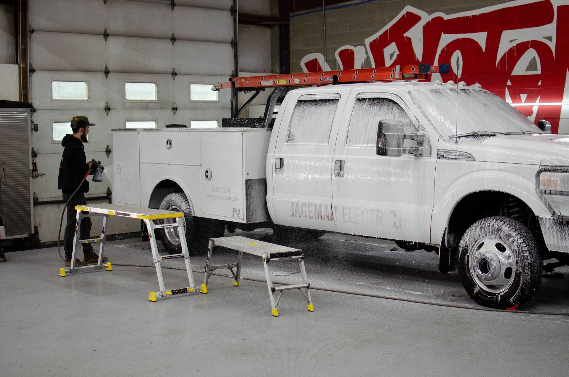 White pickup truck in a garage with a person inspecting it and two stools nearby