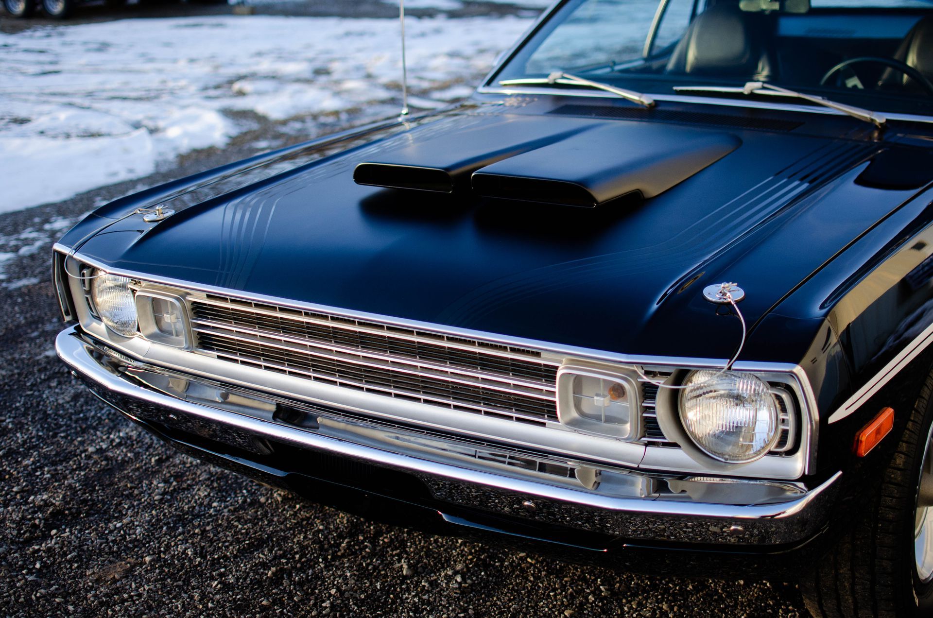 Classic black car with chrome grille parked on a snowy roadside.