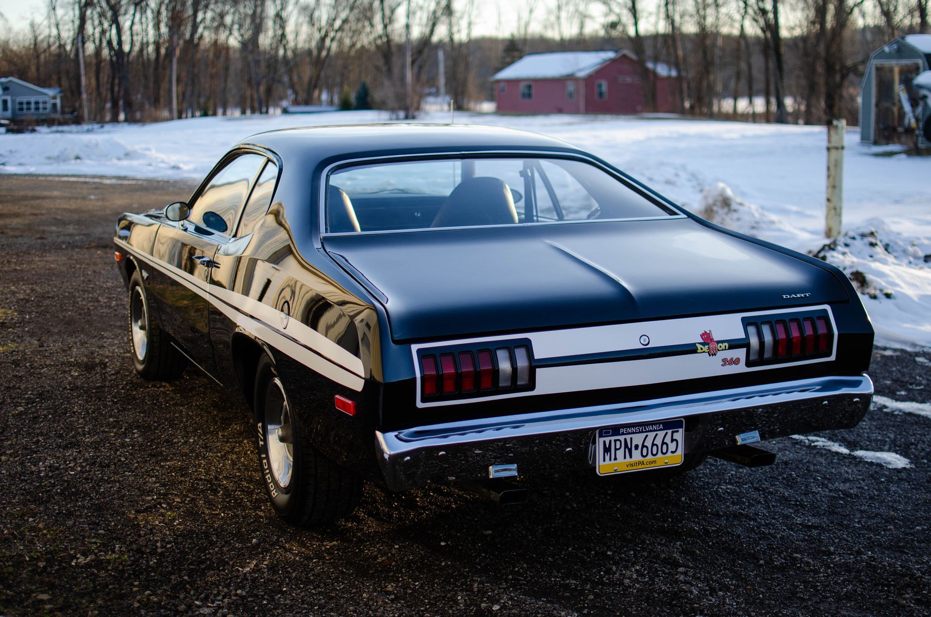 Classic black muscle car parked on a snowy roadside at dusk
