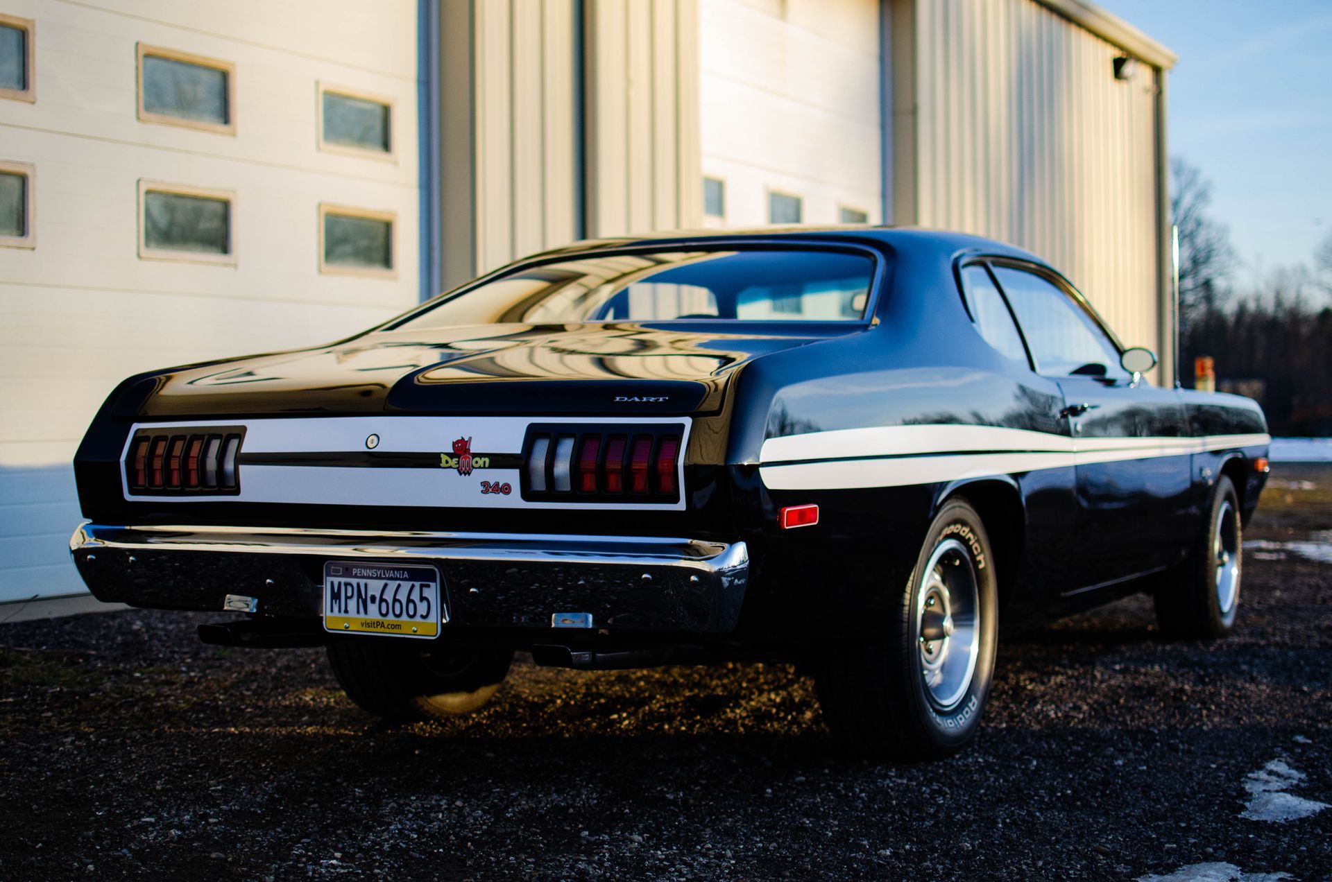 Black classic muscle car parked outside an industrial building at dusk
