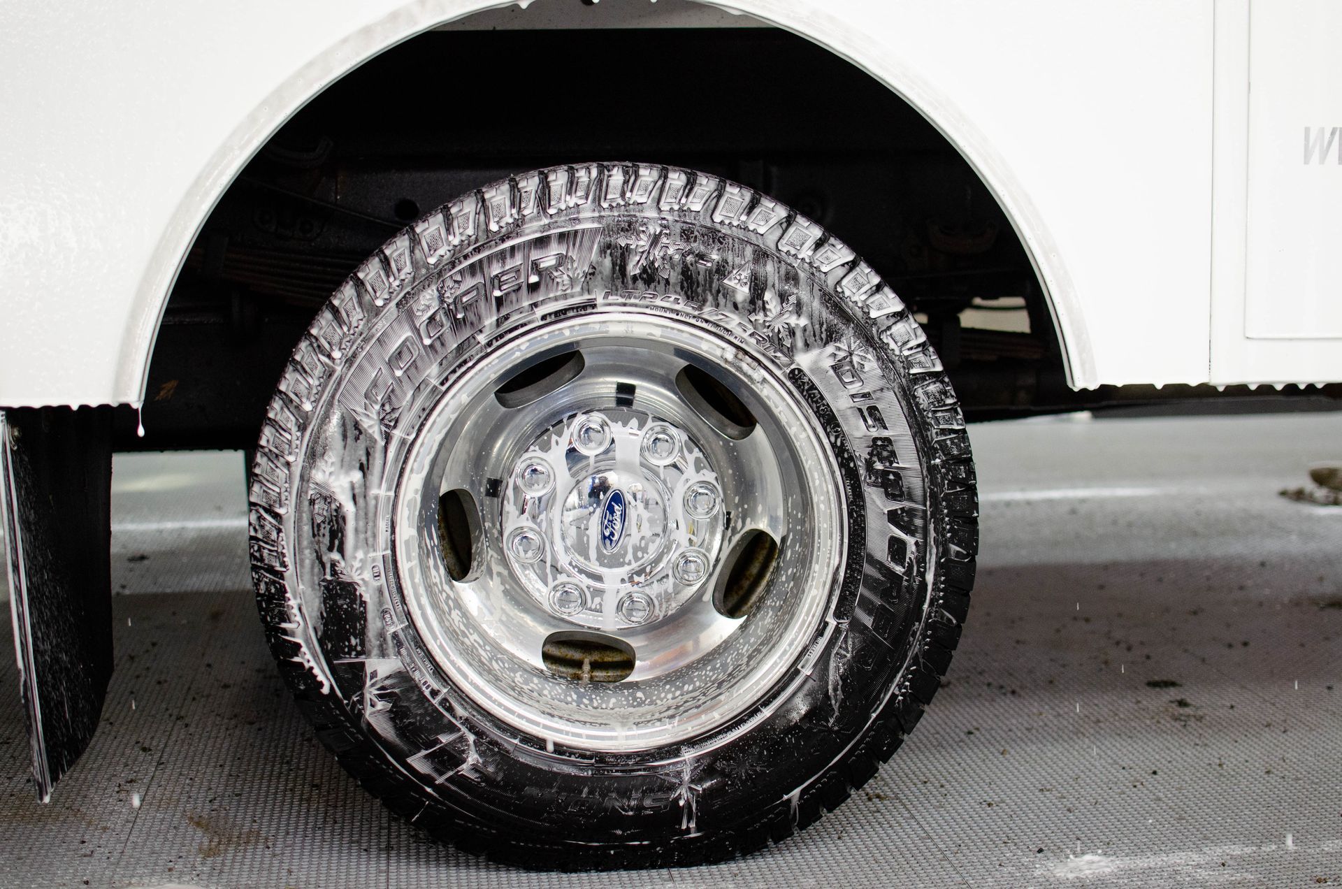 Close-up of a white truck’s rear wheel with a chrome rim on a wet road